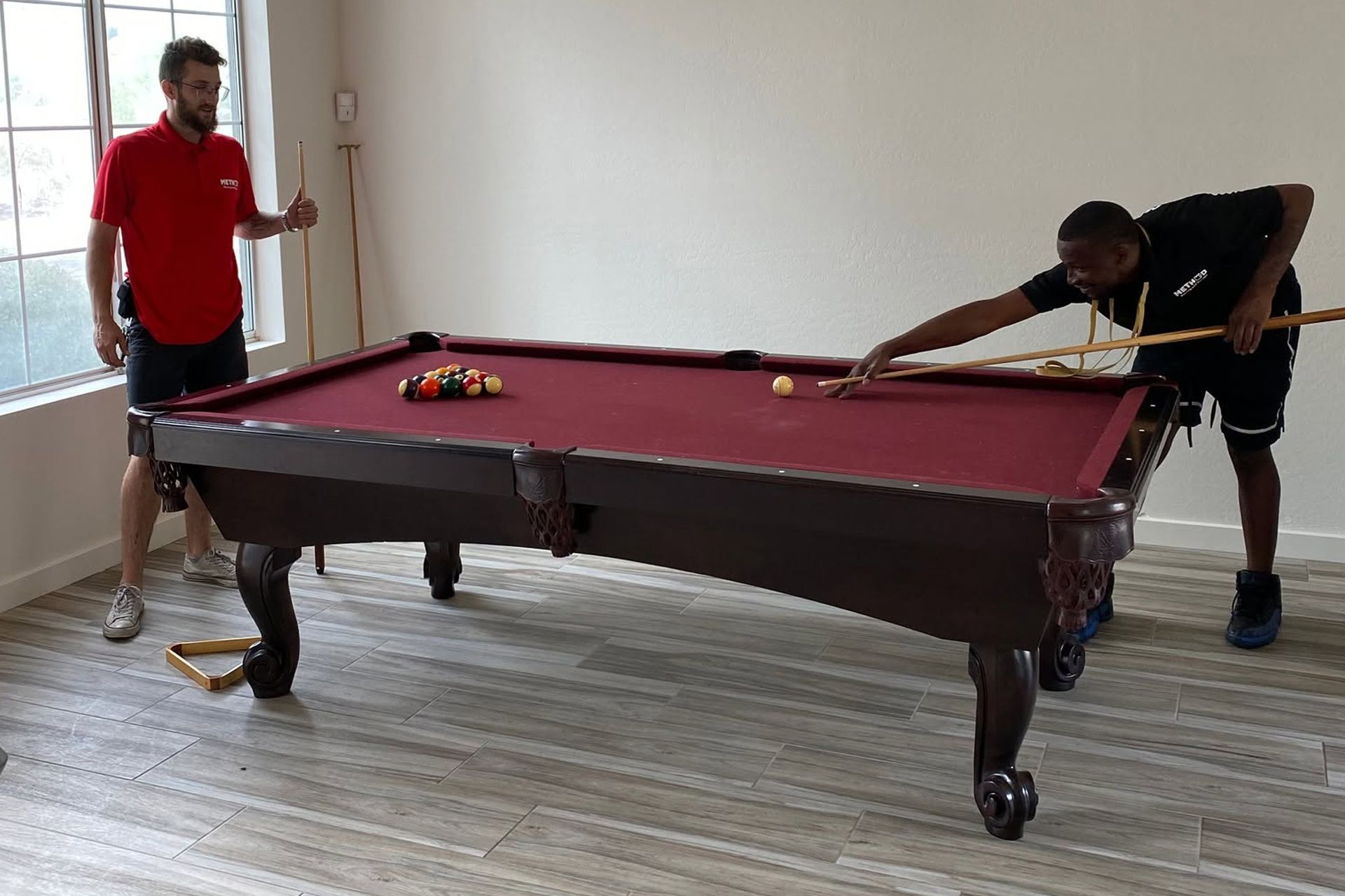 Two men positioning a maroon pool table in a bright room