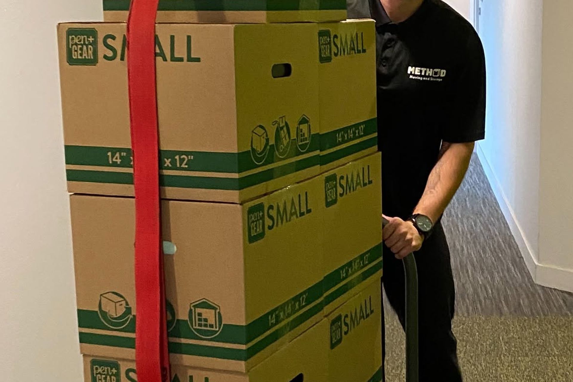 Person standing behind stacked moving boxes secured with a red strap in a hallway