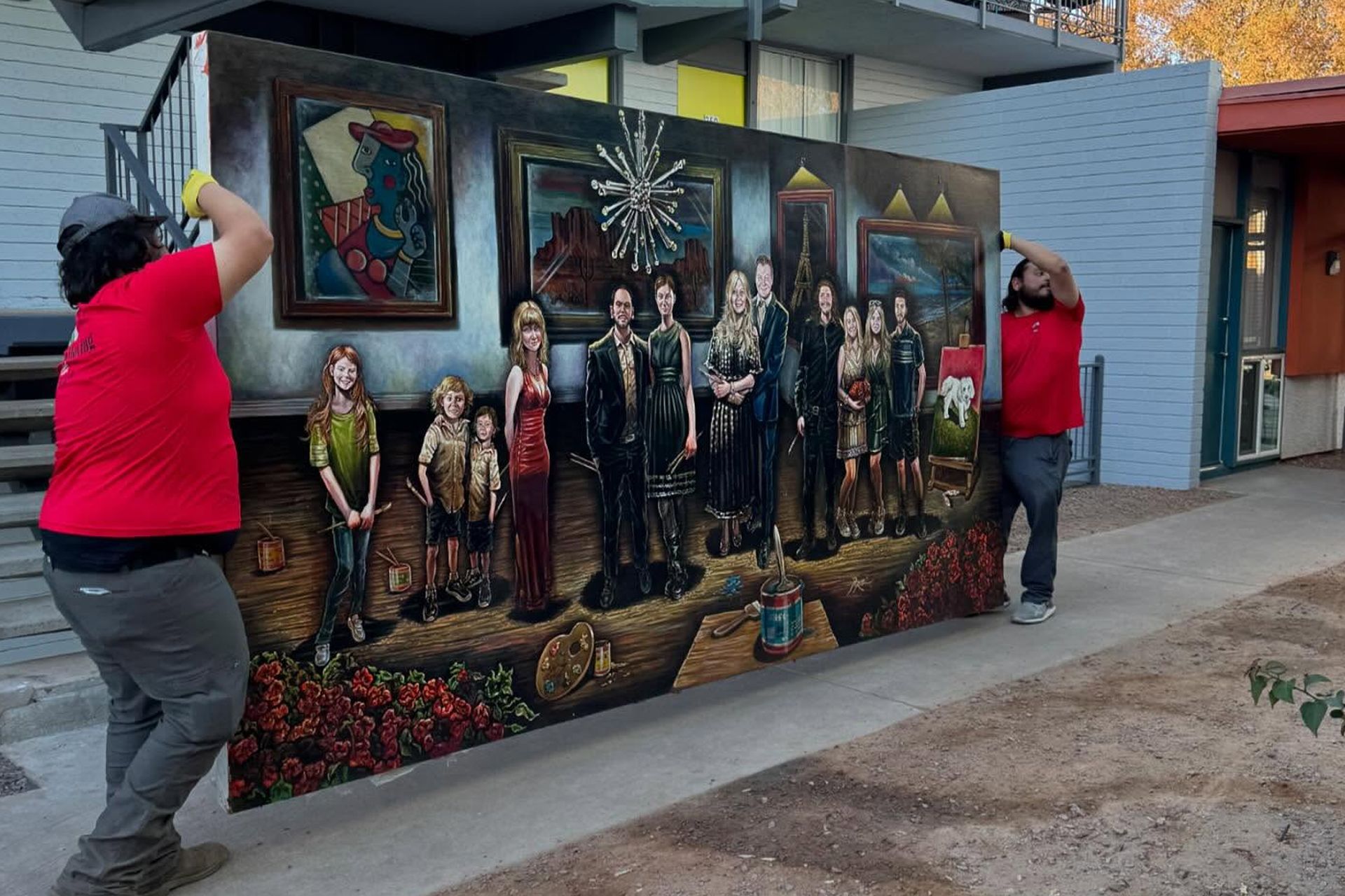 Two people in red jackets stand beside a colorful outdoor mural on a building wall.