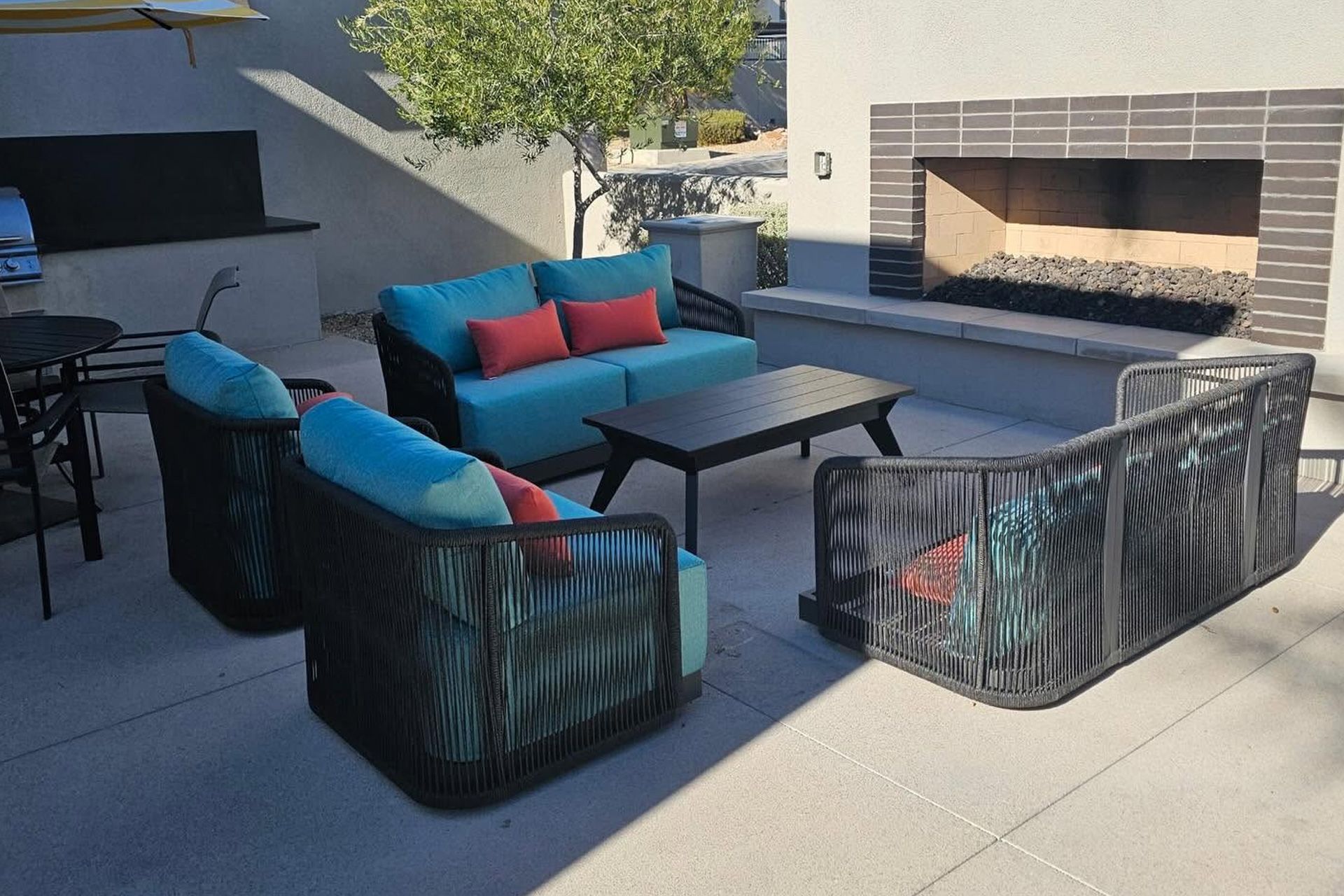 Outdoor patio seating with black wicker sofas, turquoise and red cushions, and a fire pit near a brick fireplace.