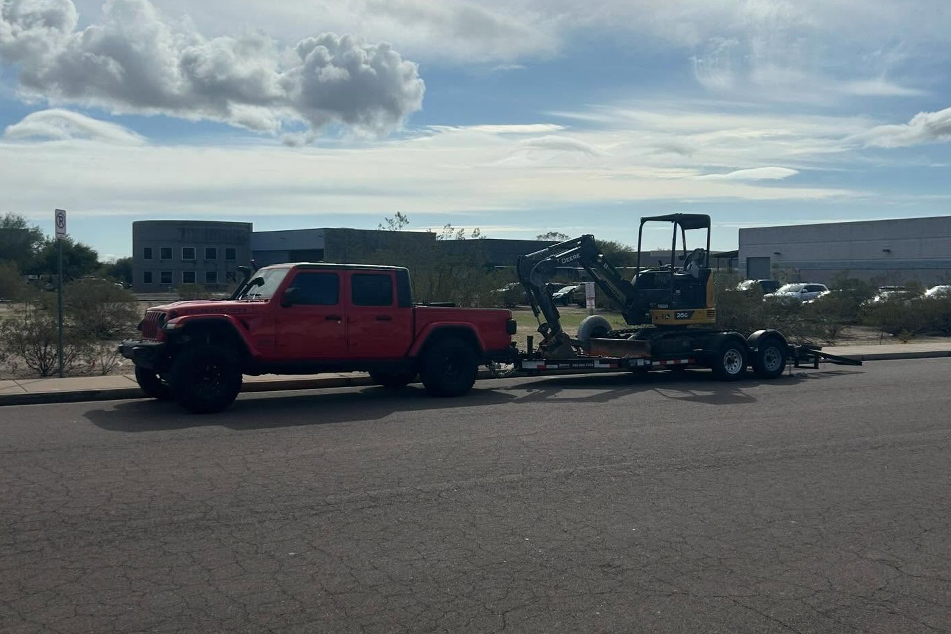 Red pickup truck towing a trailer with a mower on a roadside under a cloudy sky