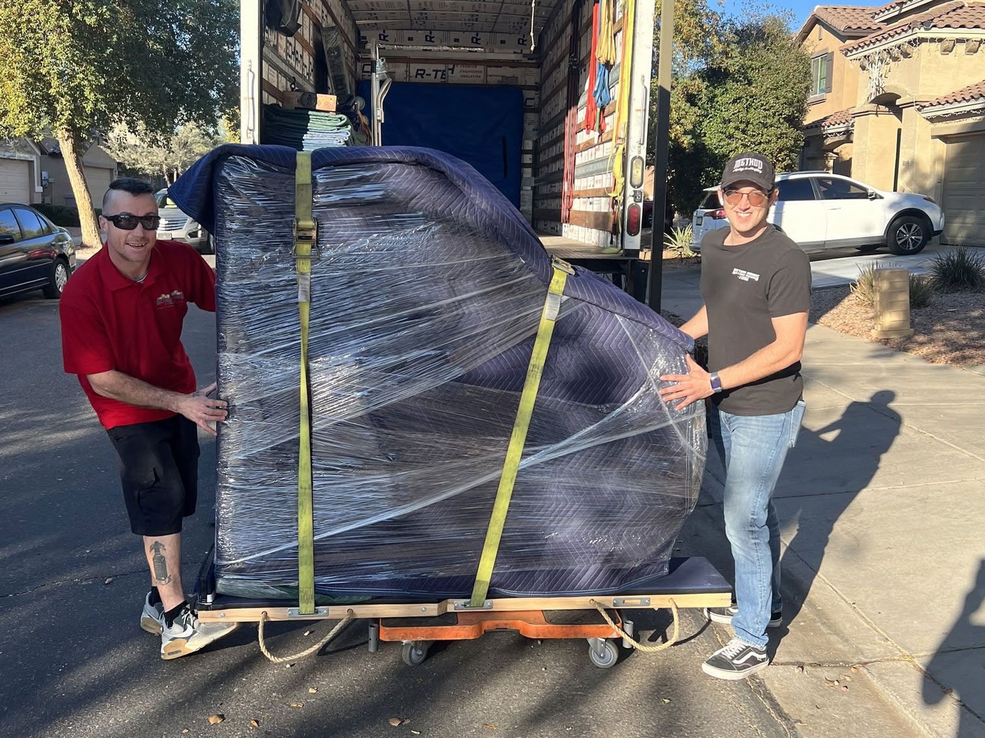 Two people unloading a large wrapped pallet from a truck on a residential street.