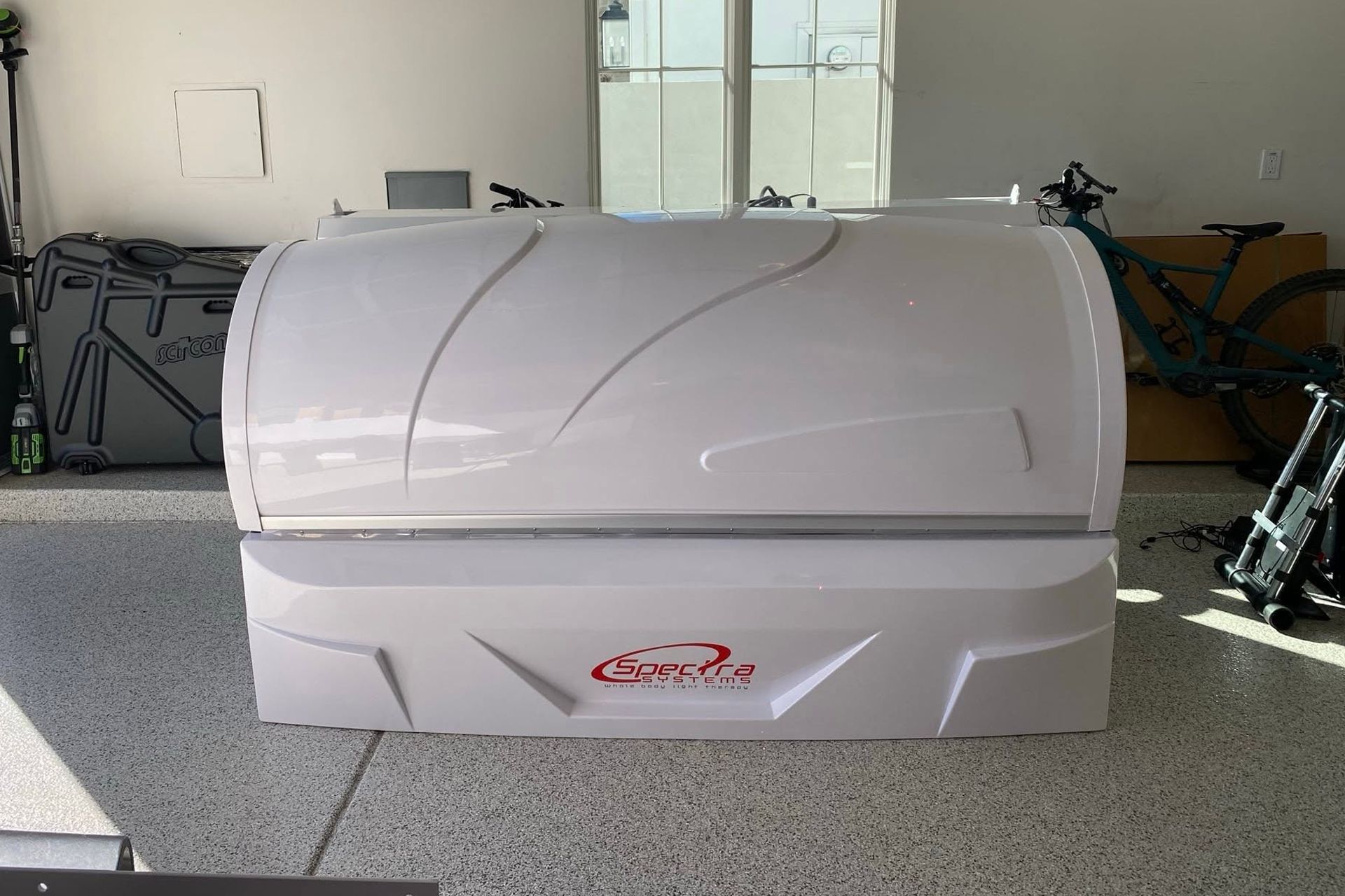 White tanning bed in a garage or showroom with speckled floor and equipment in the background