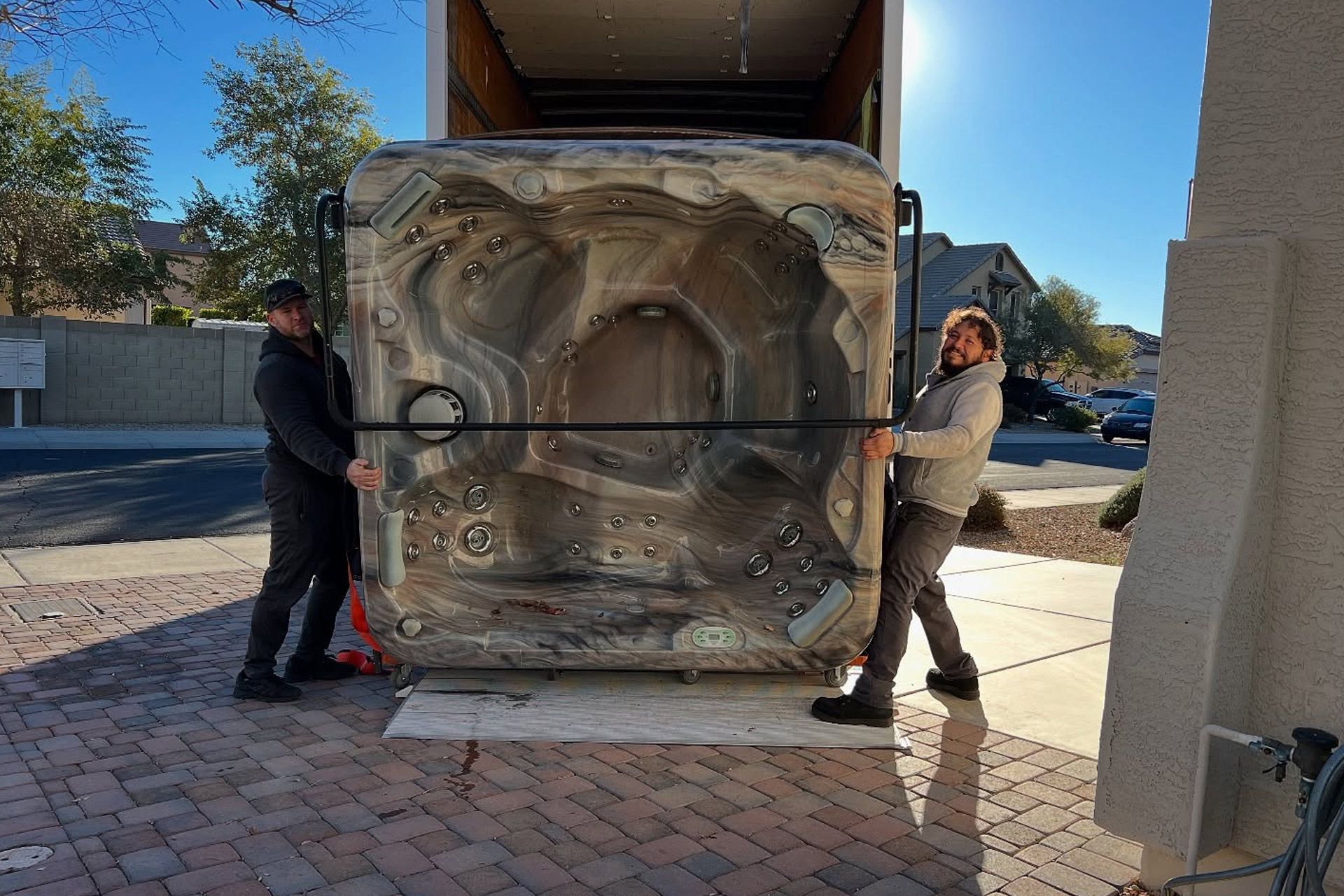 Two workers move a large wrapped crate with a dolly outside a building.