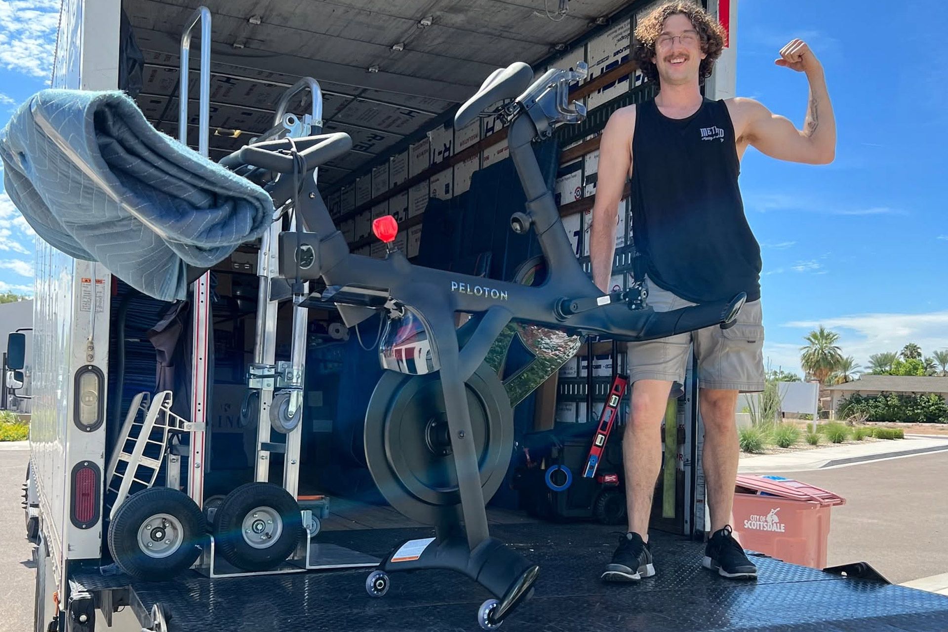 Person flexing beside gym equipment on a flatbed truck under a blue sky