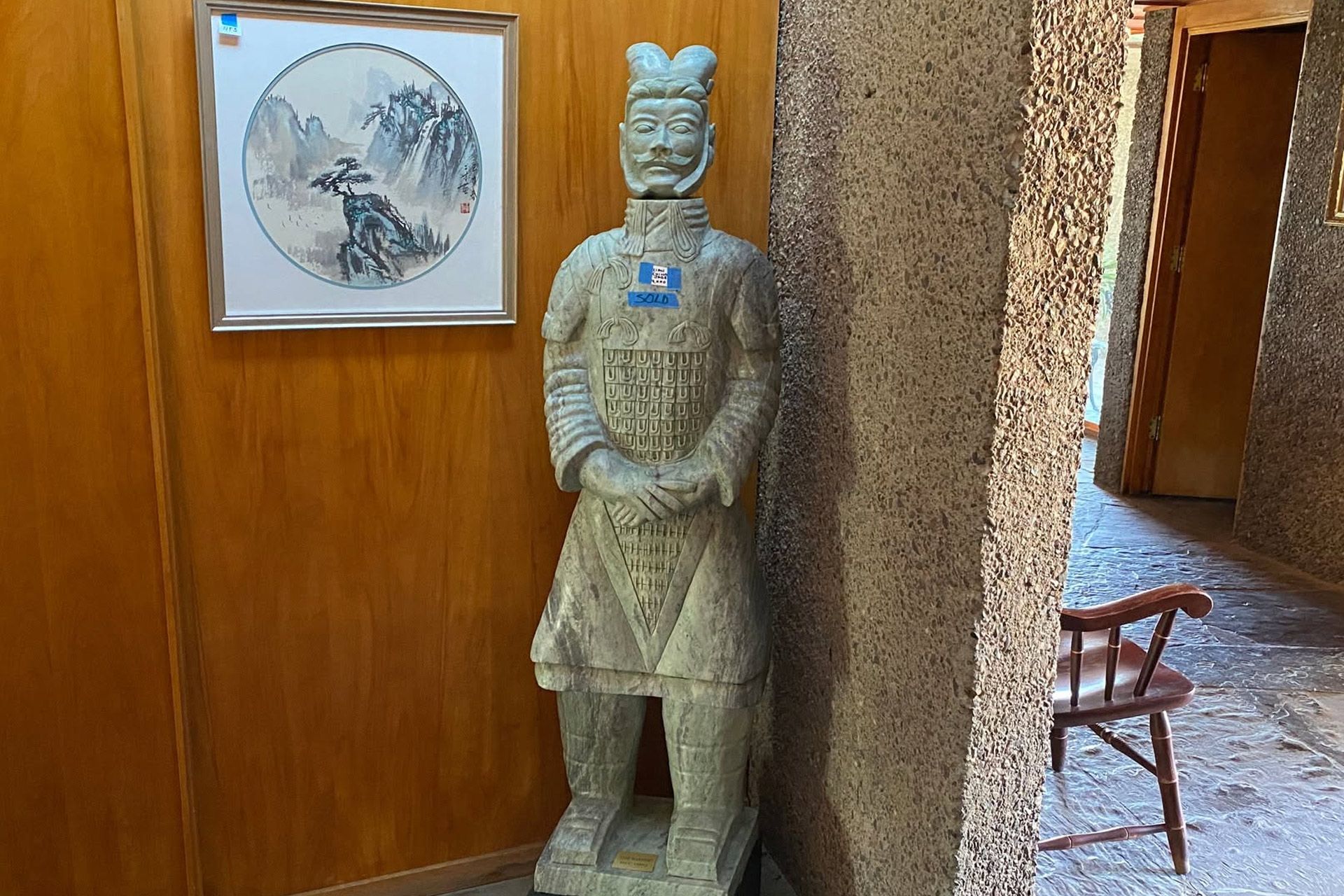 Stone warrior statue beside a framed artwork in a wooden hallway