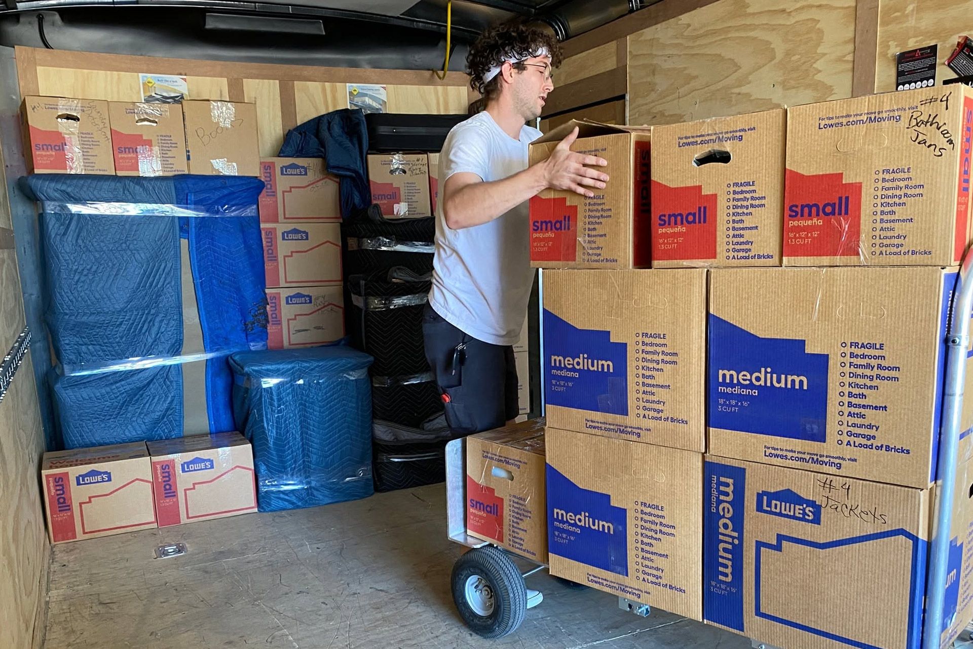 Person moving stacked cardboard boxes in a storage area with a hand truck