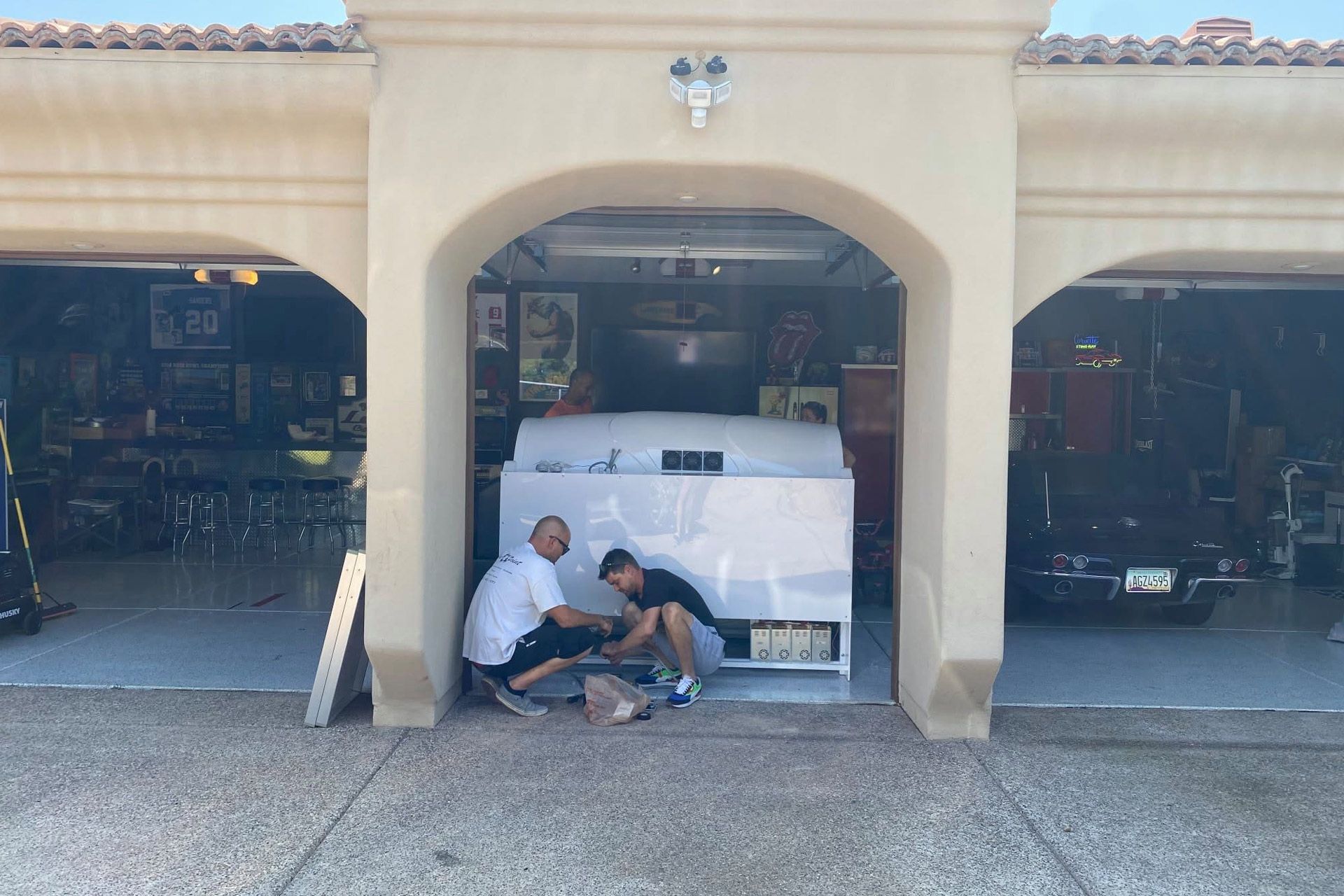 Two people crouch beside a white car under an arched garage entrance.