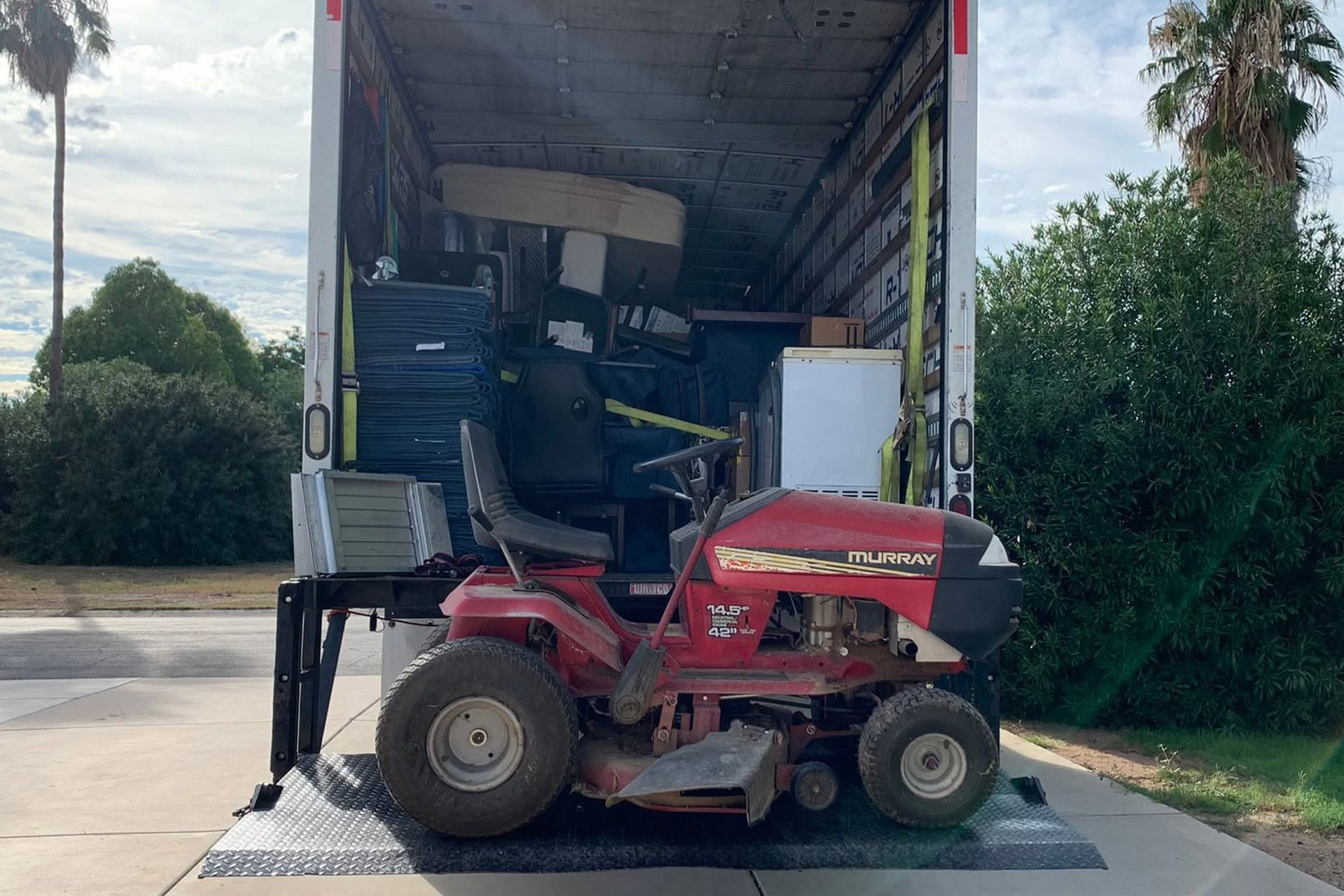 Red riding lawn mower on a truck ramp, partially loaded into a box truck with landscaping equipment inside.