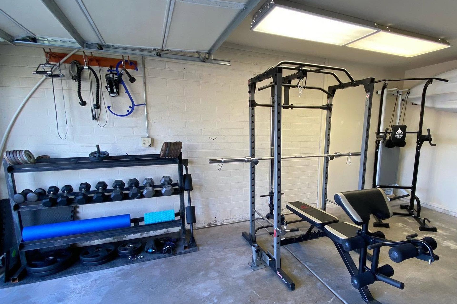 Garage gym with dumbbell rack, weight machine, bench, and wall-mounted equipment