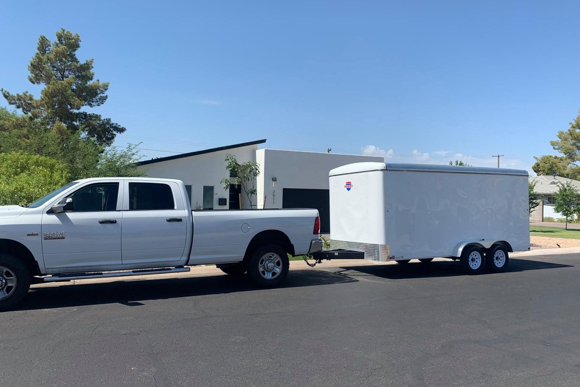 White pickup truck towing a white enclosed trailer on a sunny street