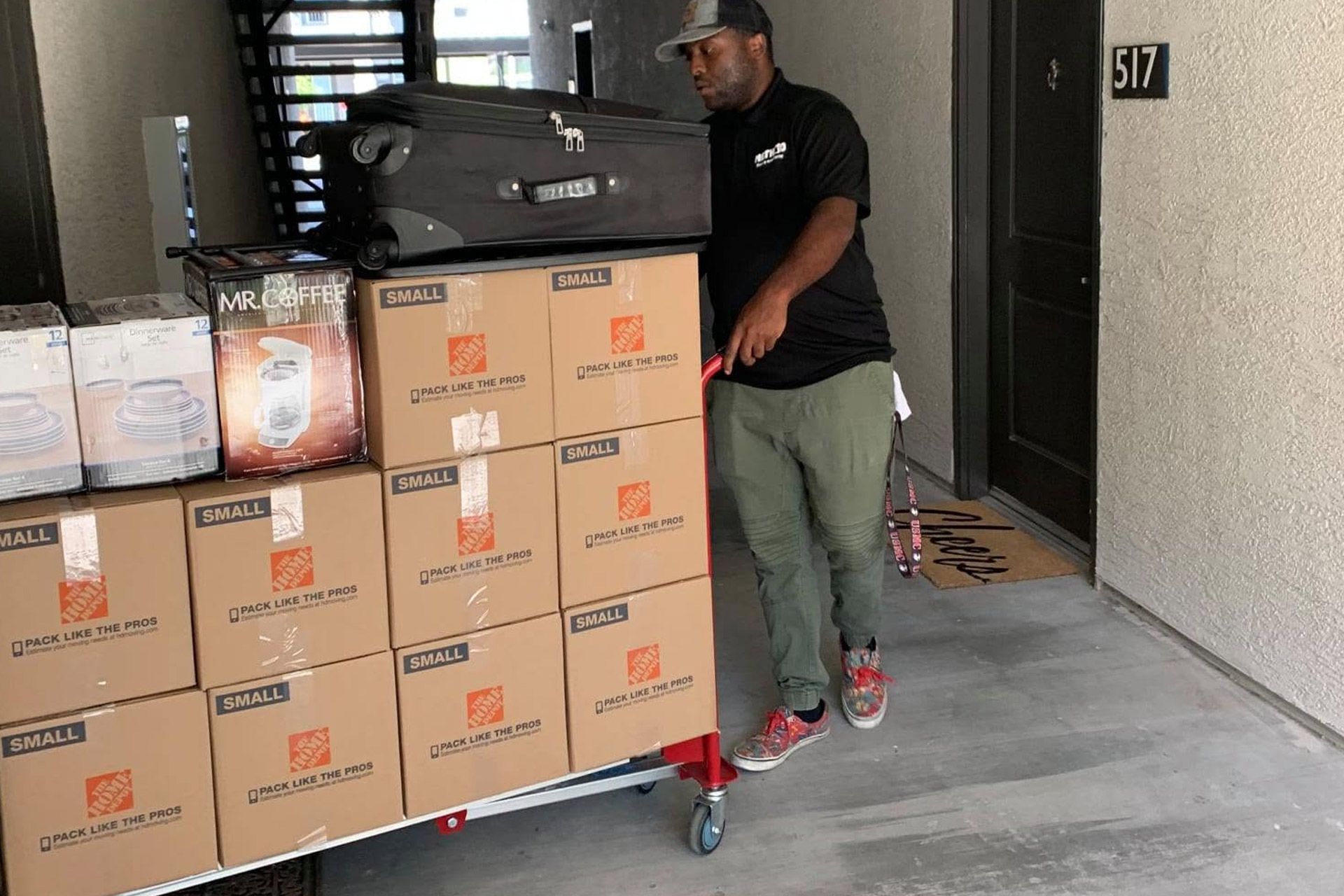 Man pushing a dolly stacked with cardboard boxes in an apartment hallway