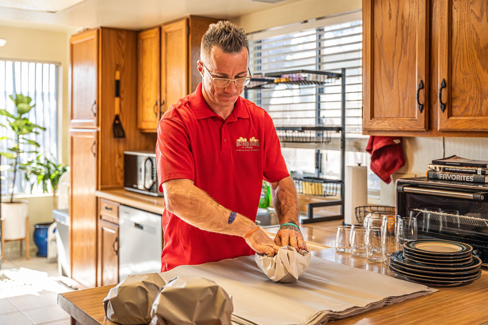 Man in red shirt arranging dough on a kitchen counter in a bright home kitchen