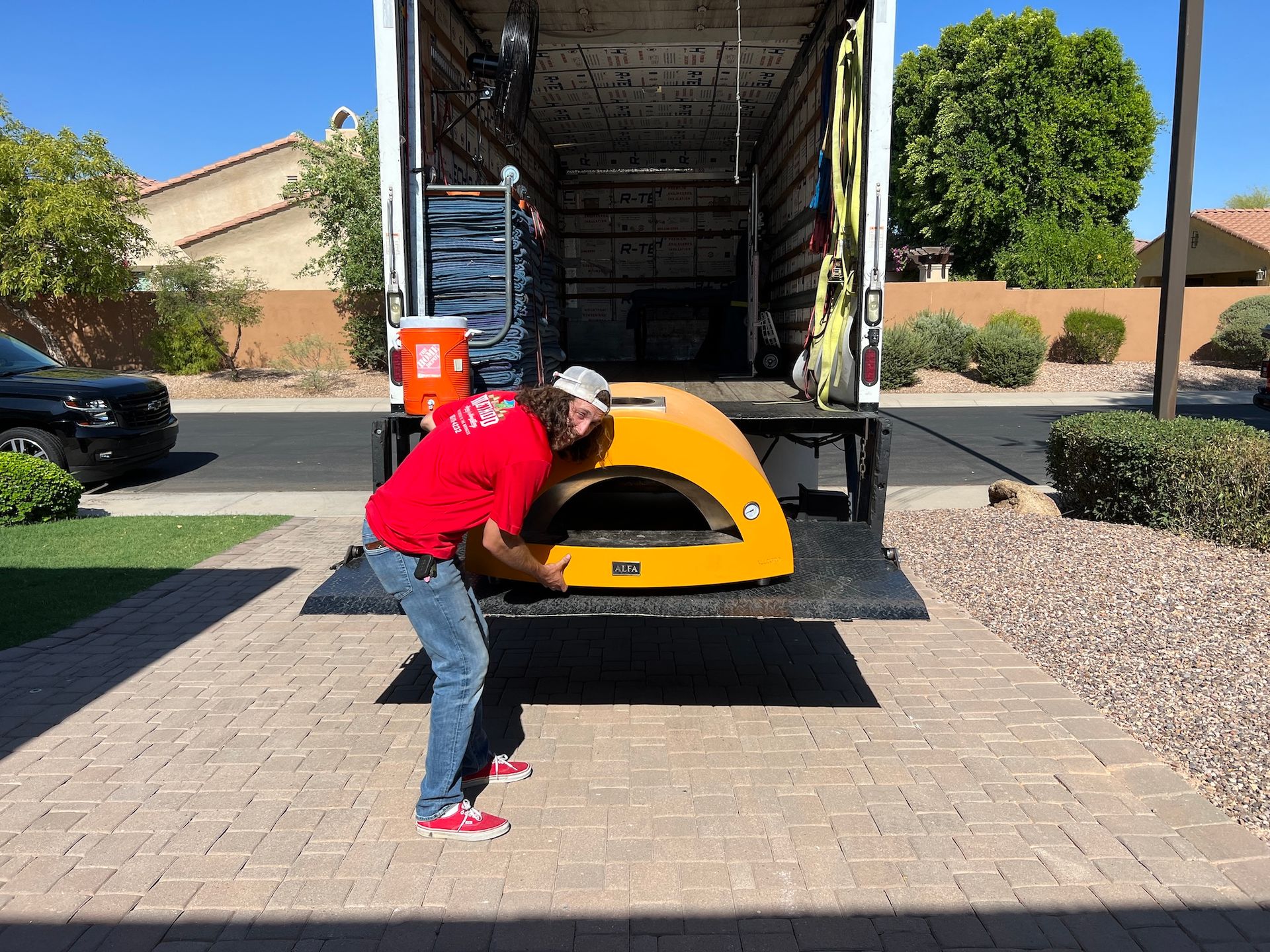 Man in red shirt unloading a yellow object from a truck in a driveway