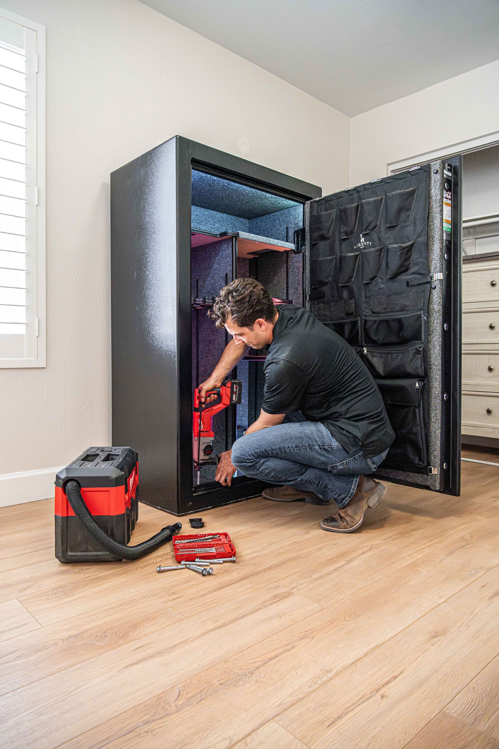 Person working inside open black cabinet in a room, with red tool bag on the floor