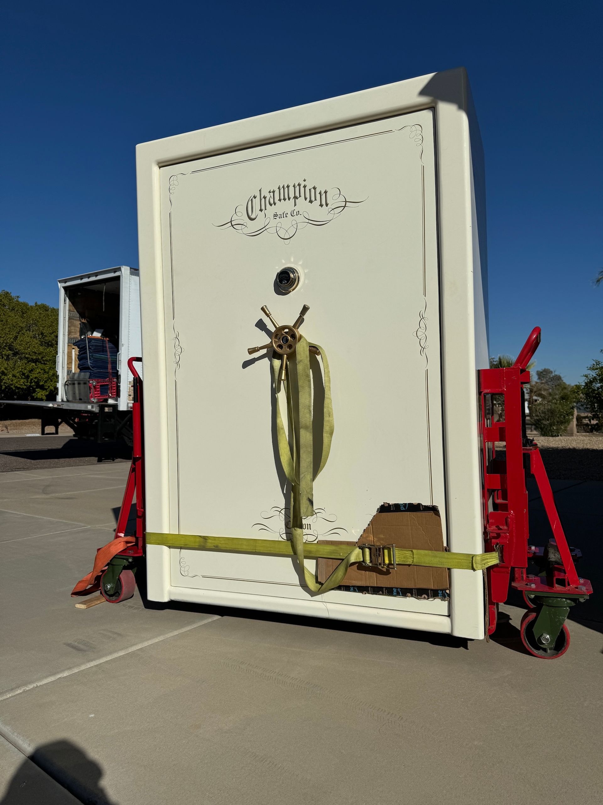 Large white metal box secured with straps on a red trailer in a sunny parking lot