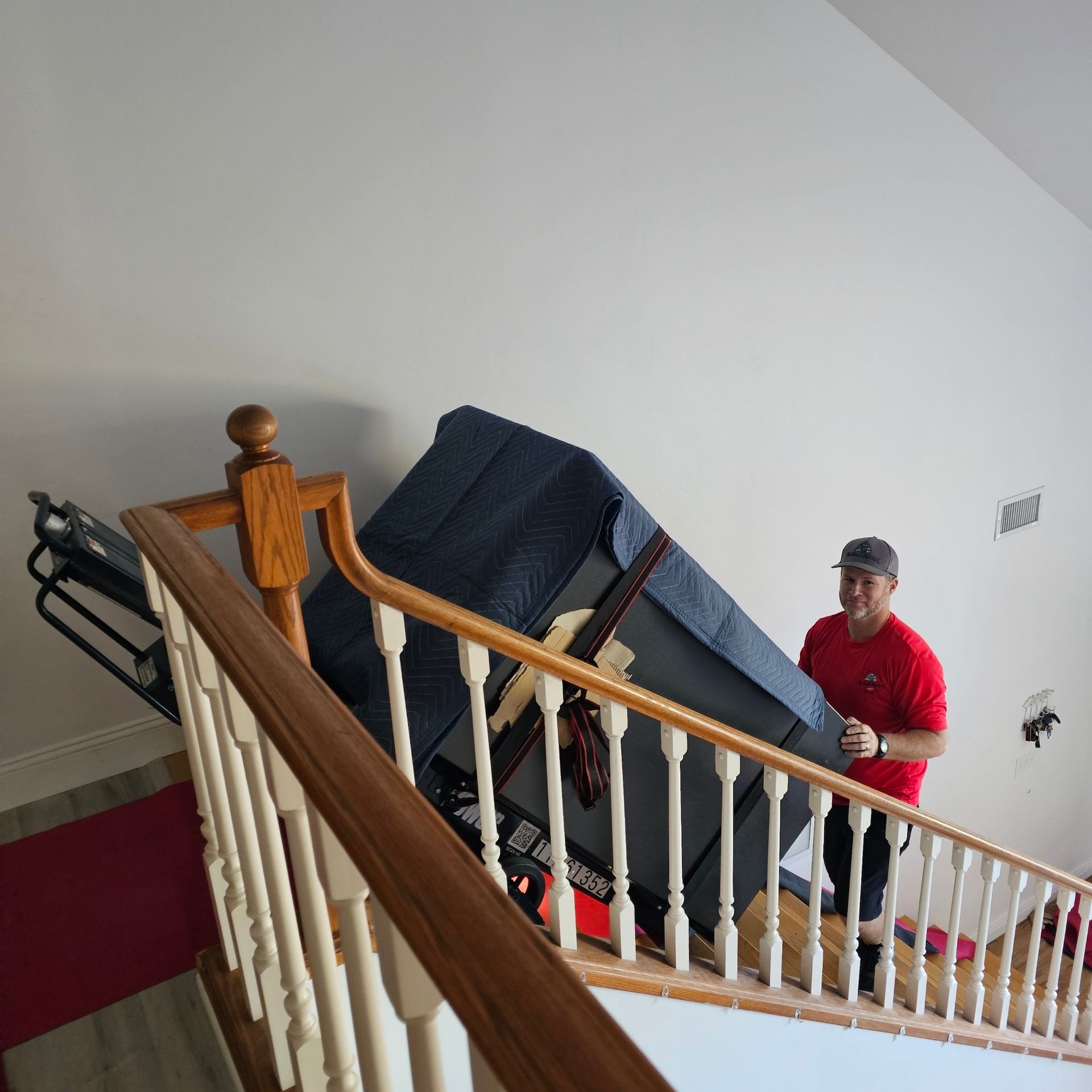 Two people carrying a large couch up a staircase in a narrow indoor hallway