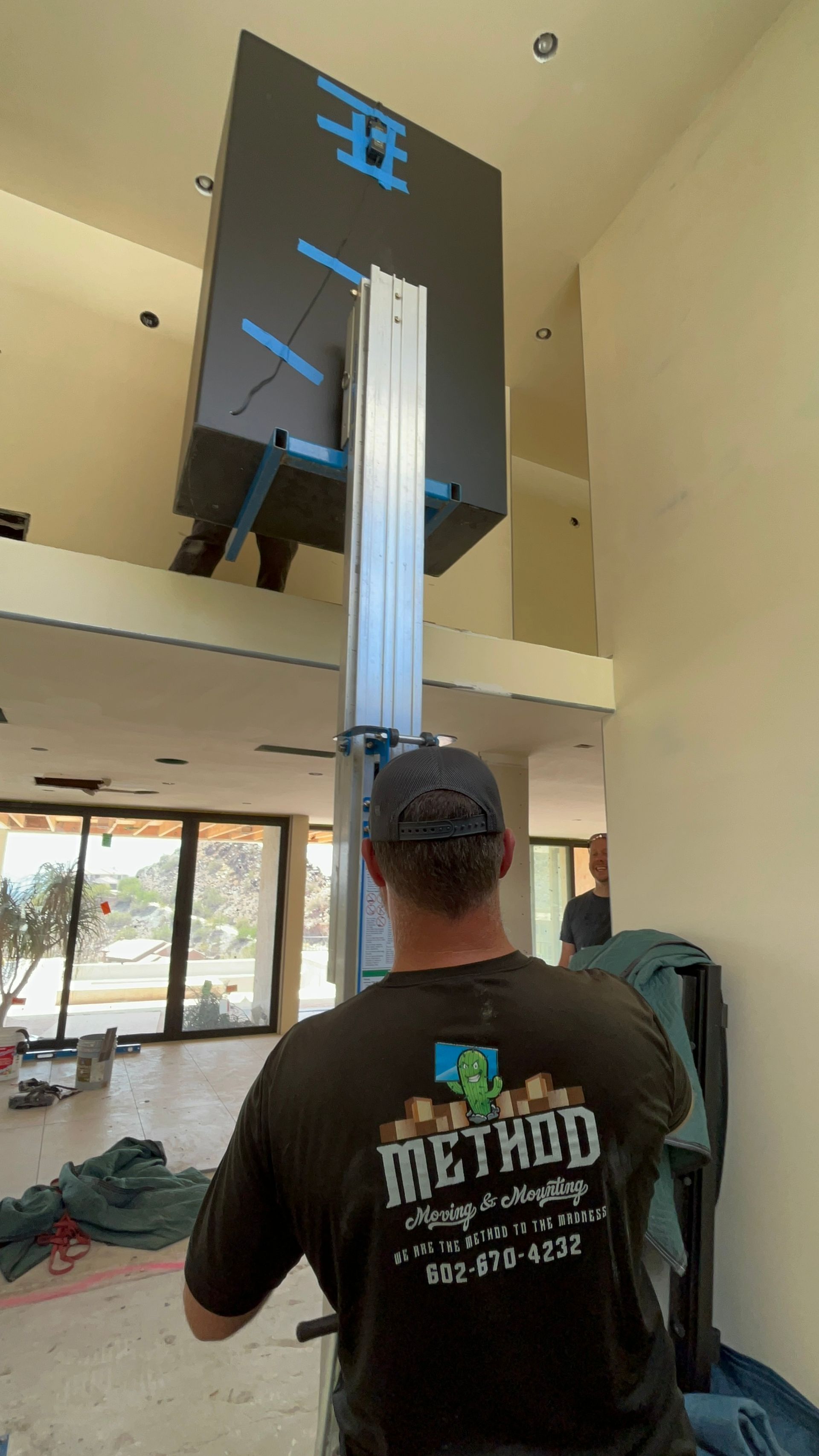 Person stands indoors beneath a hanging black digital sign in a bright lobby.