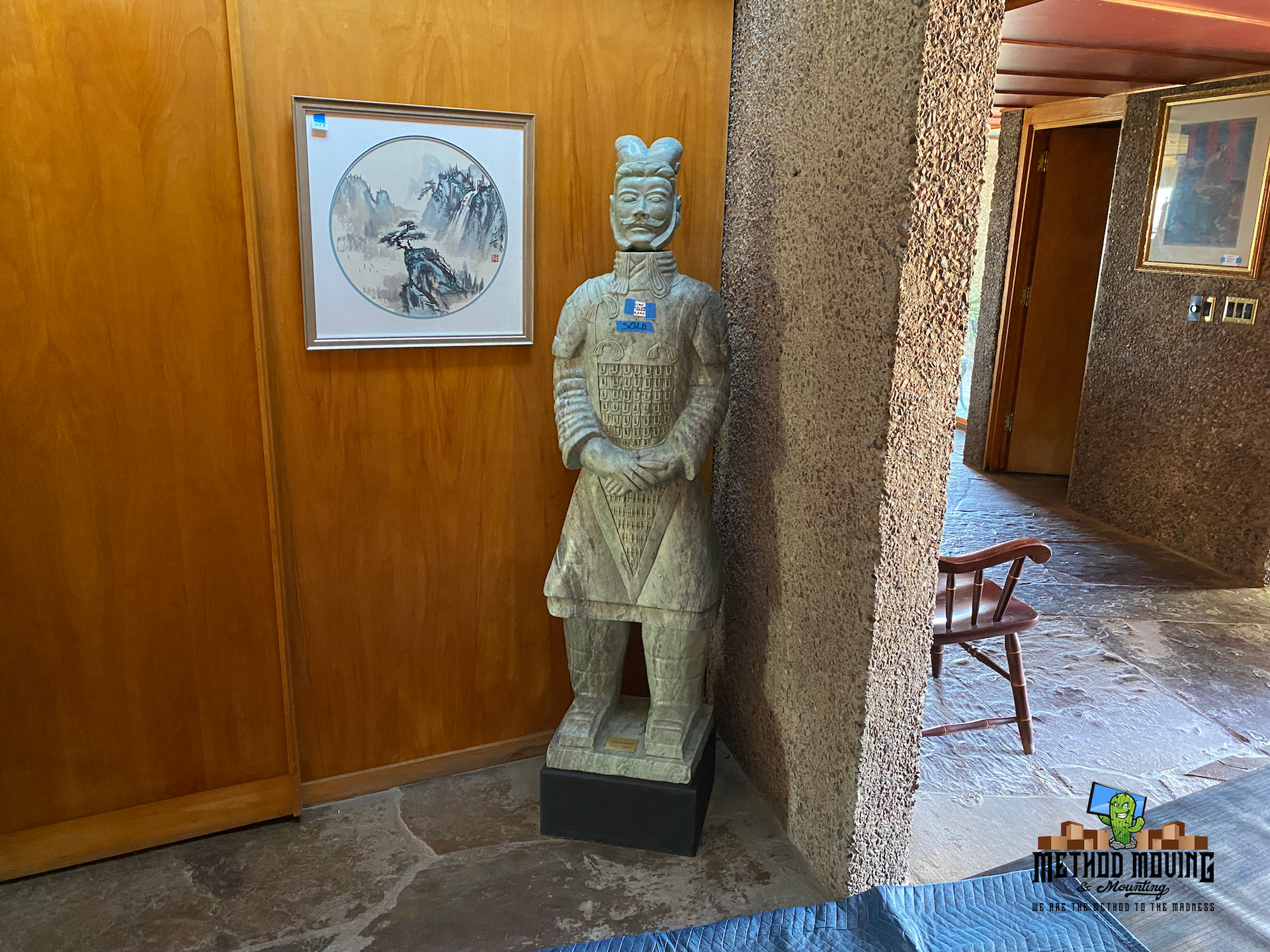 Stone statue by a wooden wall in a hallway, beside a framed artwork and open doorway.