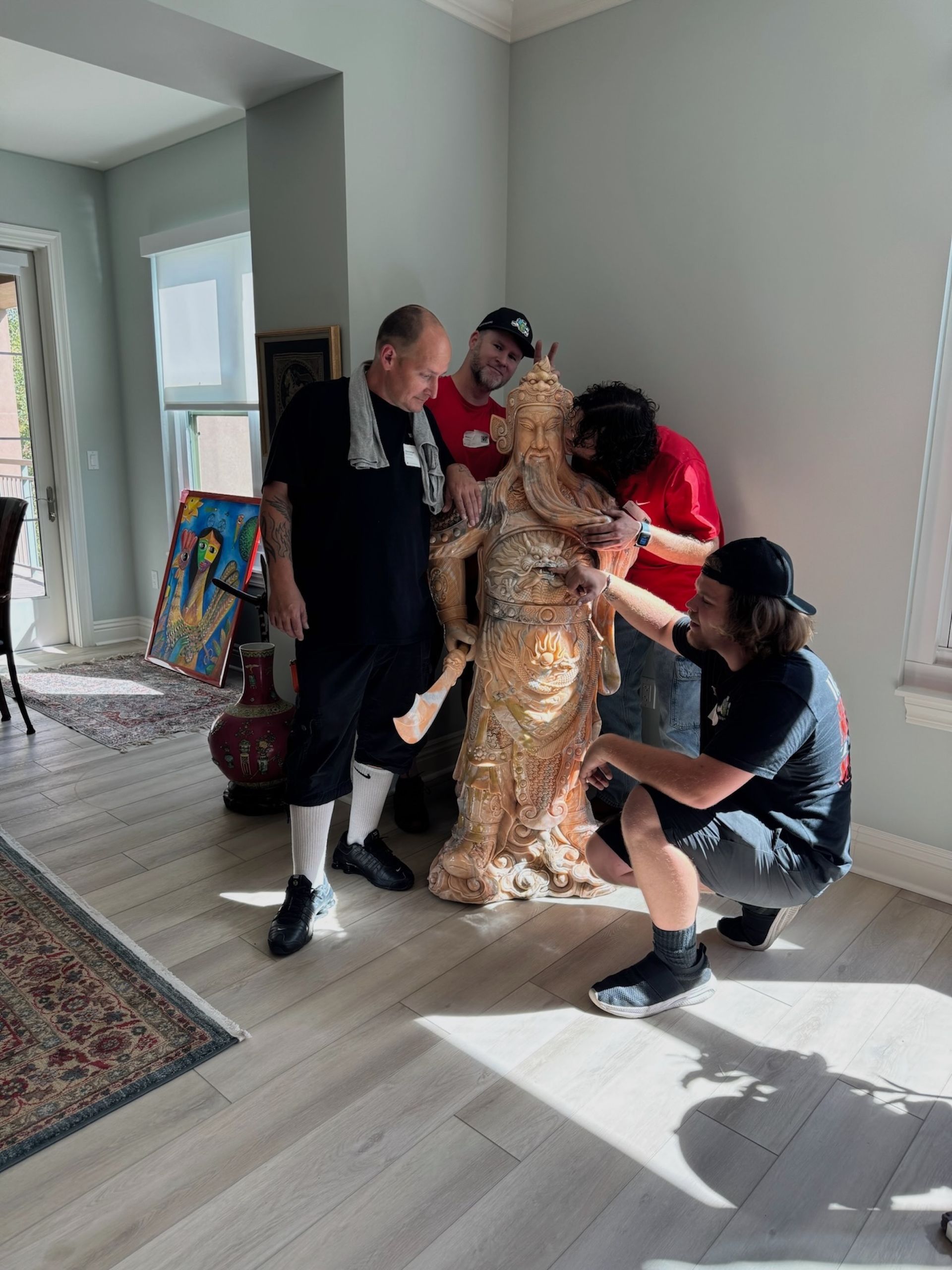 People gathered in a bright room, helping someone in a gold dress stand while a man crouches nearby.