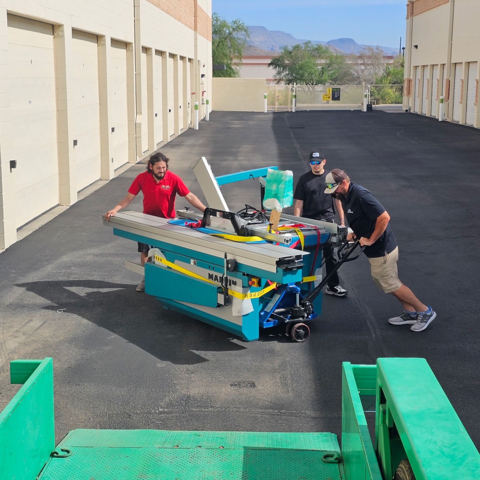 Three people push a turquoise machine in an alley between buildings.