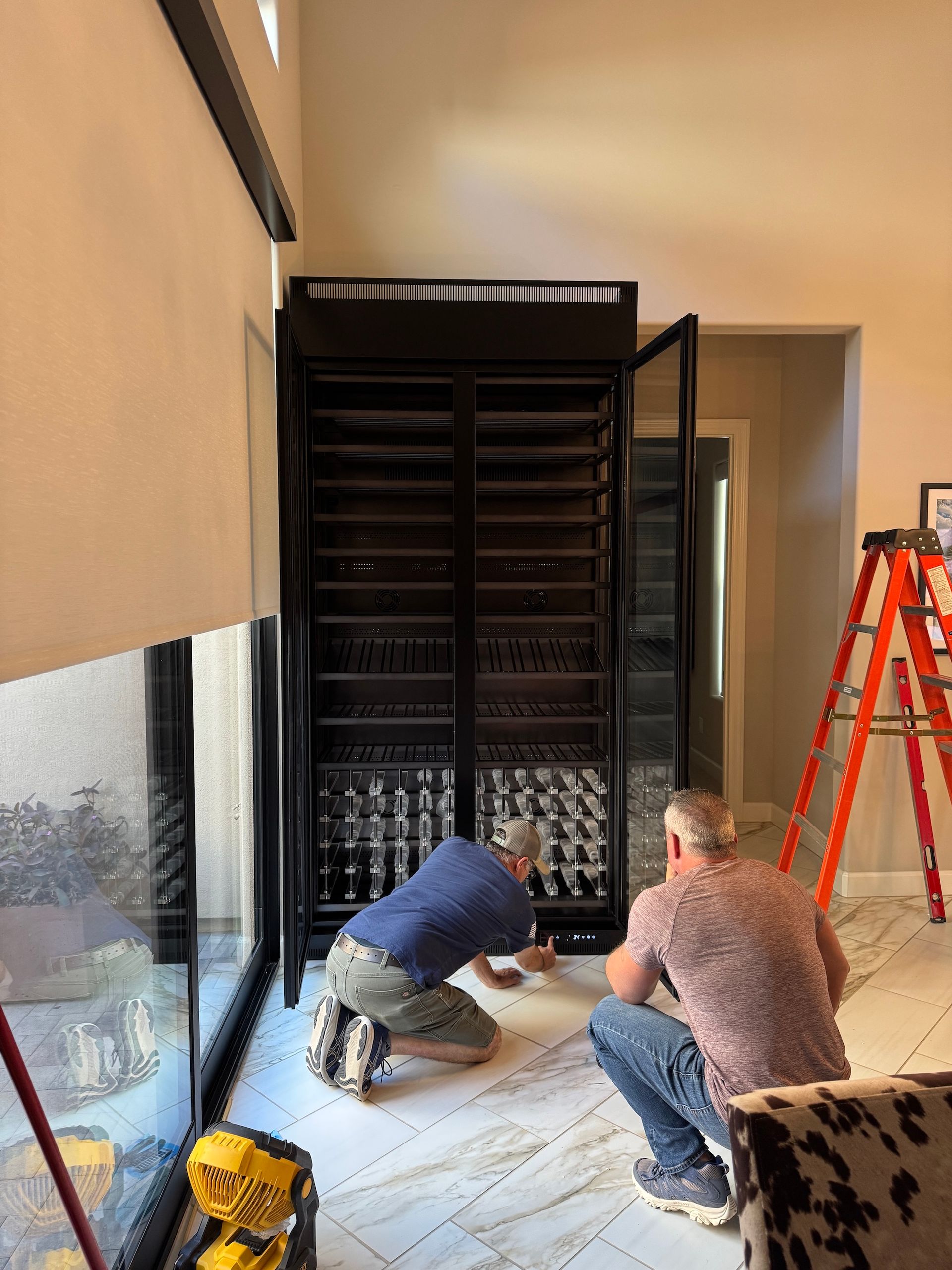 Two workers installing a large black metal gate in a hallway, with a ladder nearby.