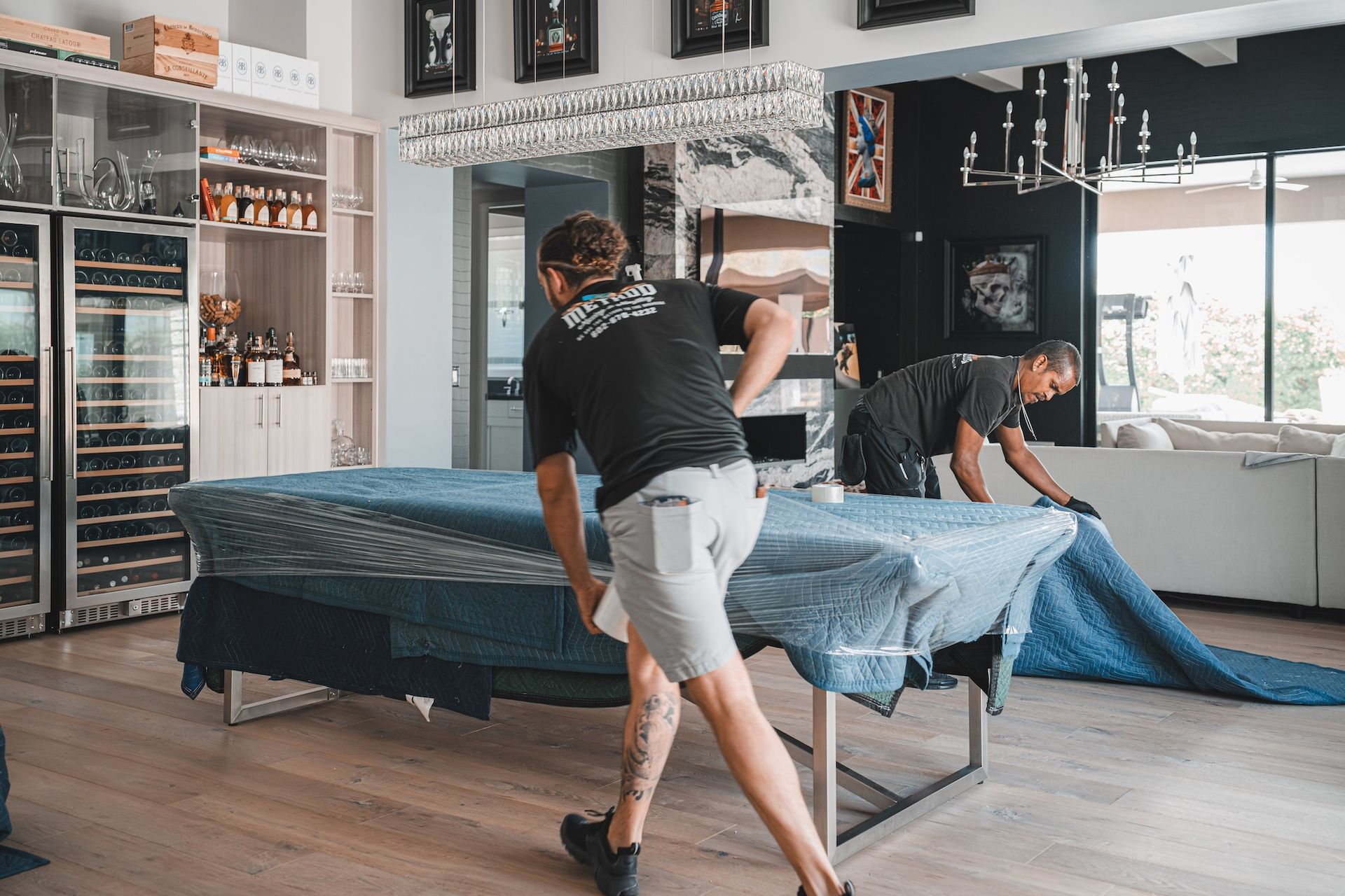 Two people making a bed with a blue cover in a bright bedroom.