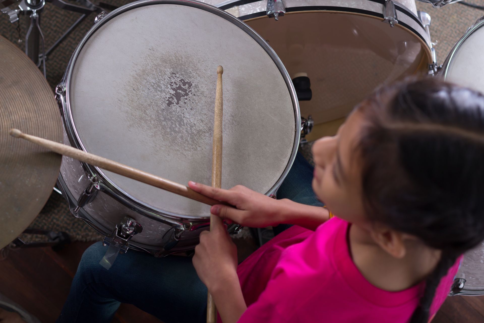 A little girl in a pink shirt is playing a drum set