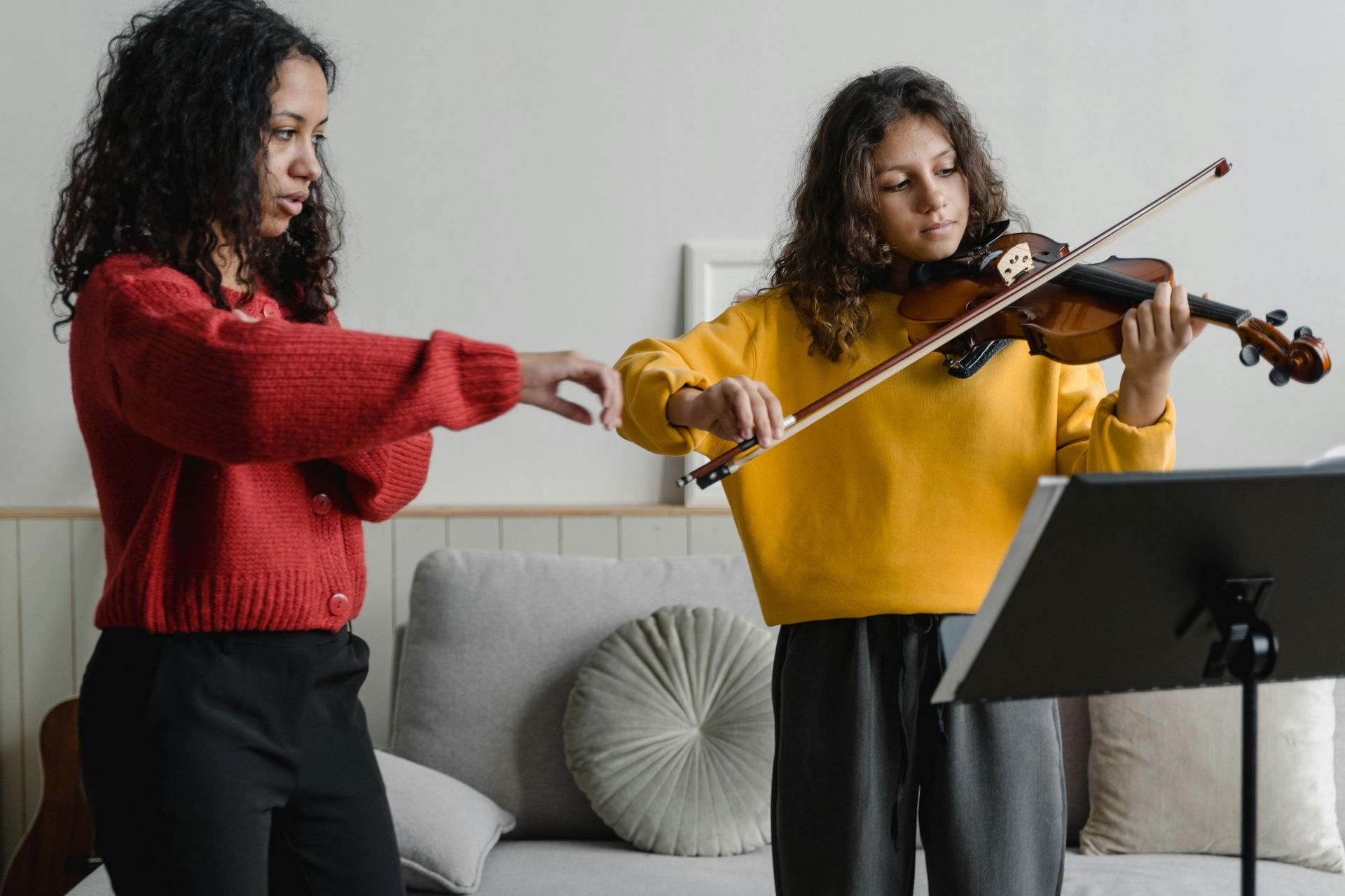 Two women are playing violins in a living room.