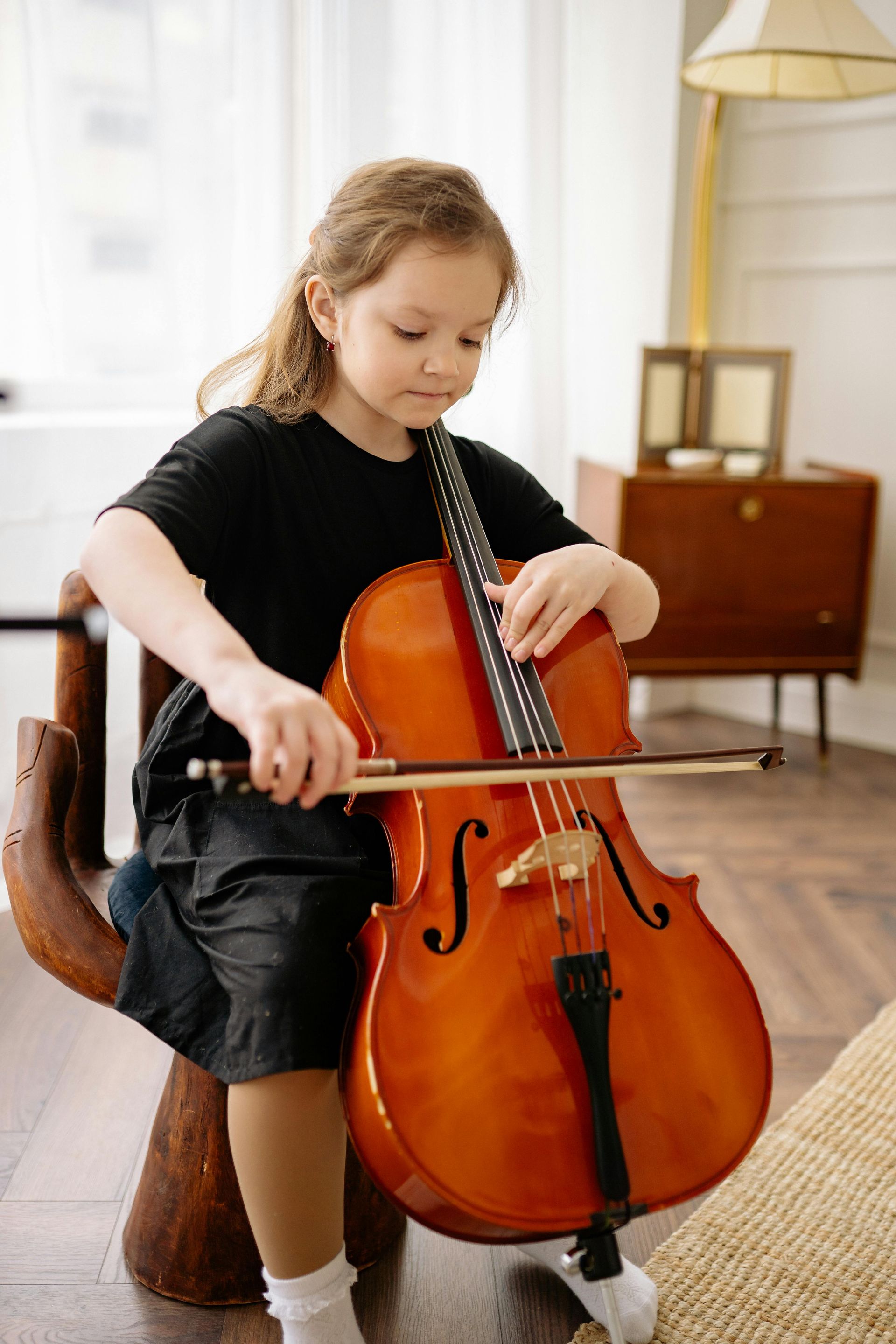 A little girl is sitting on a chair playing a cello.