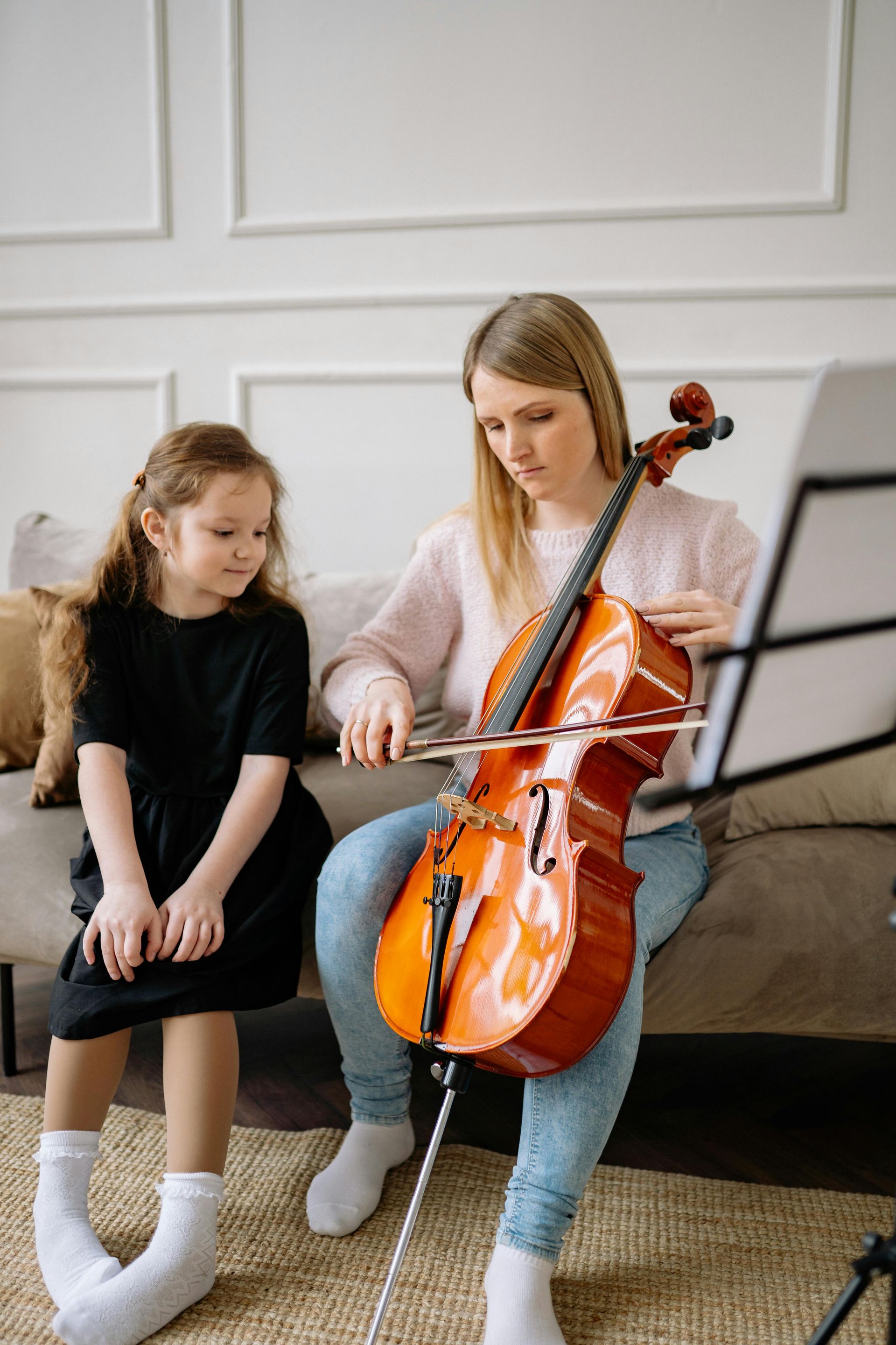 A woman is teaching a little girl how to play a cello.
