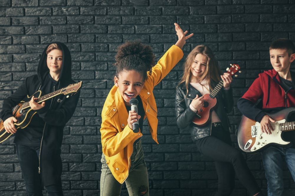 A group of young people are playing guitars and singing in front of a brick wall.