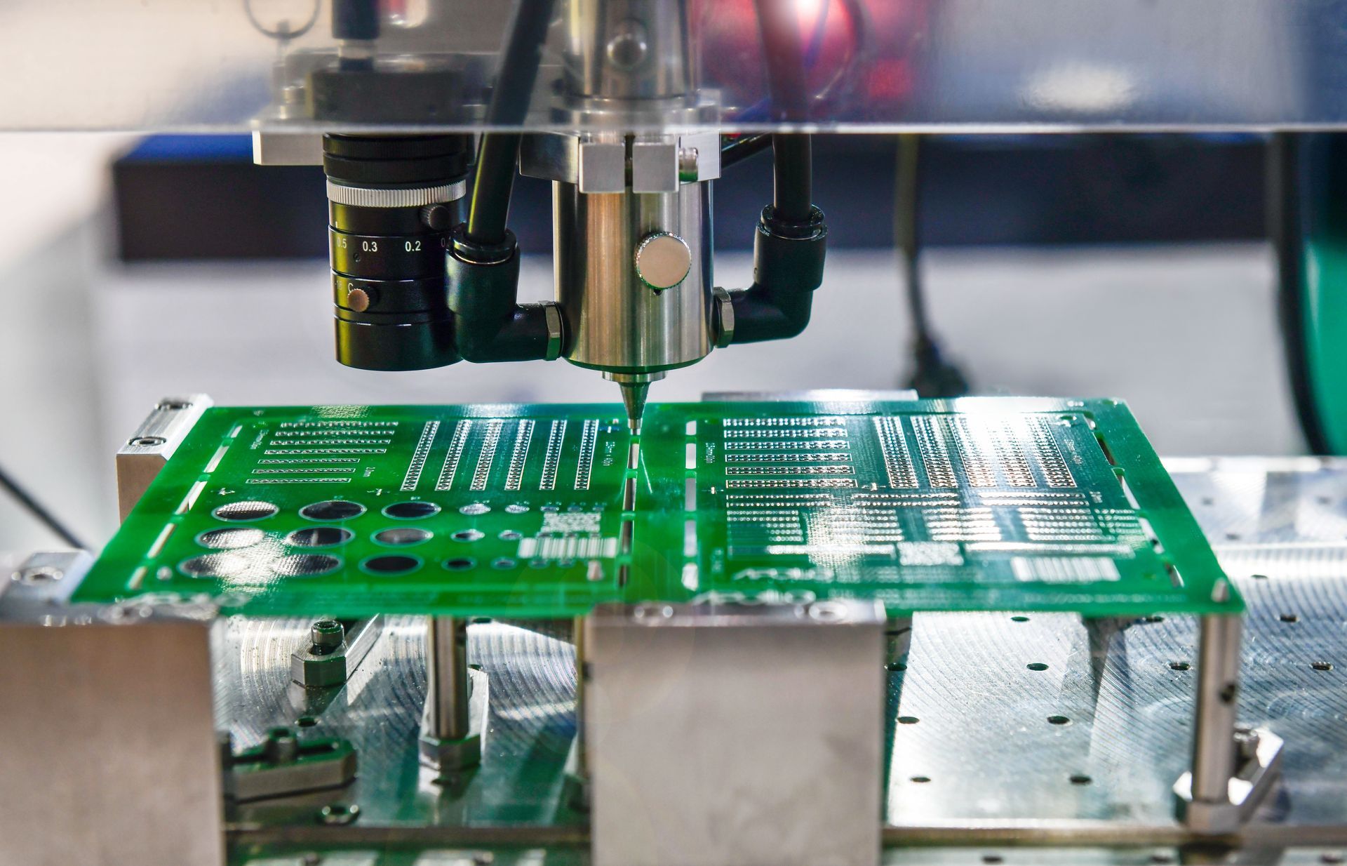 Green circuit board under a machine nozzle in a factory, being manufactured or inspected
