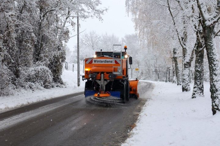 Orange snowplow clearing a snowy road lined with snow-covered trees