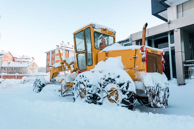 Yellow snowplow buried in deep snow on a residential street near houses