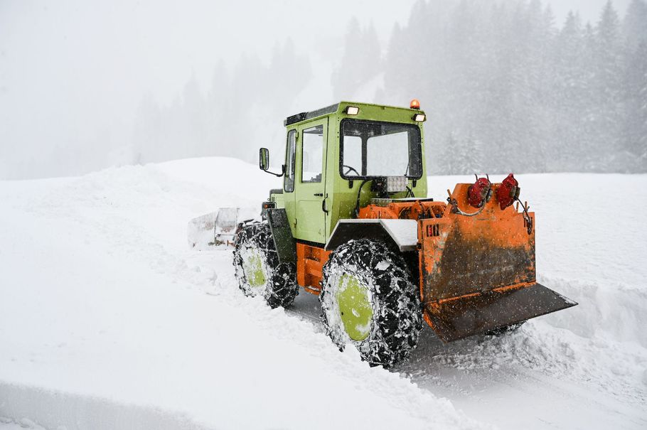 Green snowplow clearing a snowy road in a white winter landscape