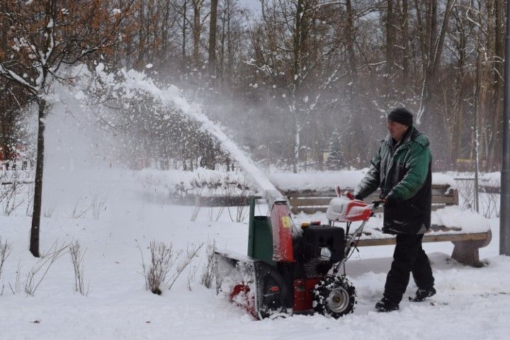 Person using a snow blower to clear snow in a snowy yard, spraying snow into the air.