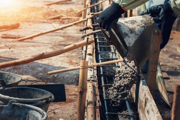 A construction worker is pouring concrete into a concrete wall.