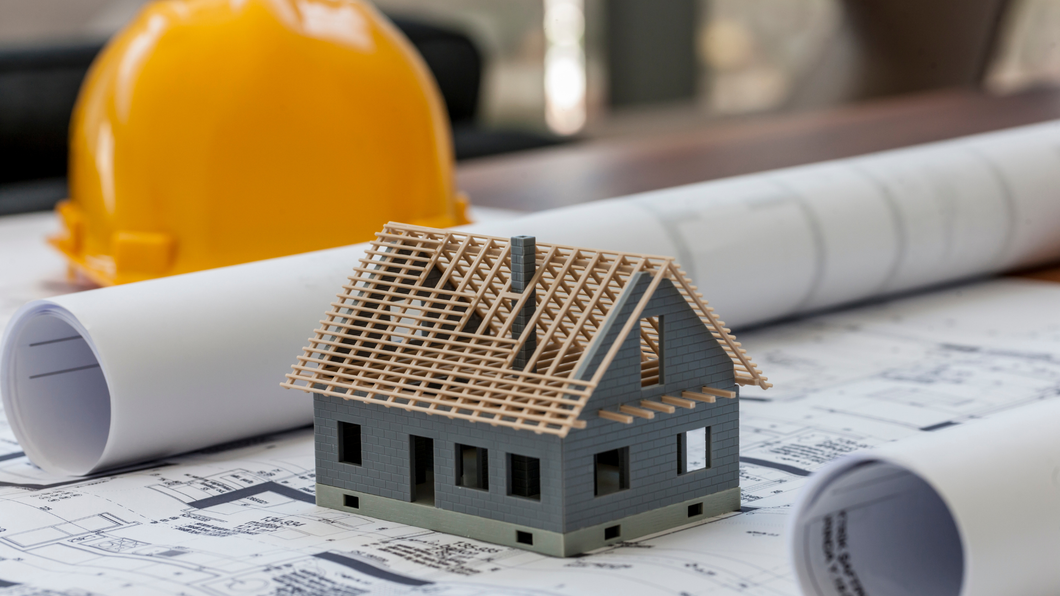 A model house is sitting on top of a blueprint next to a hard hat.