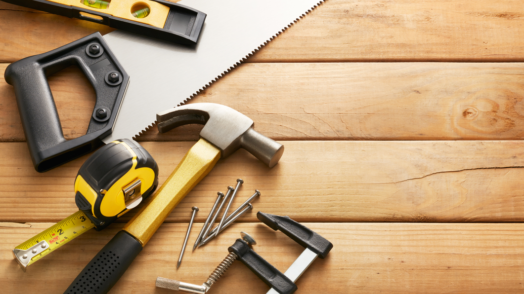 A wooden table topped with a hammer , tape measure , saw , clamp , and nails.