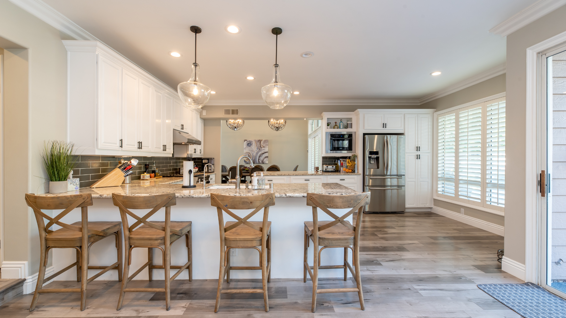 A kitchen with white cabinets , stainless steel appliances , a large island , and wooden chairs.