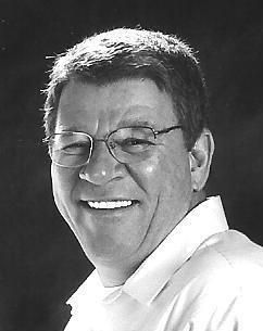 A man wearing glasses and a white shirt is smiling in a black and white photo.