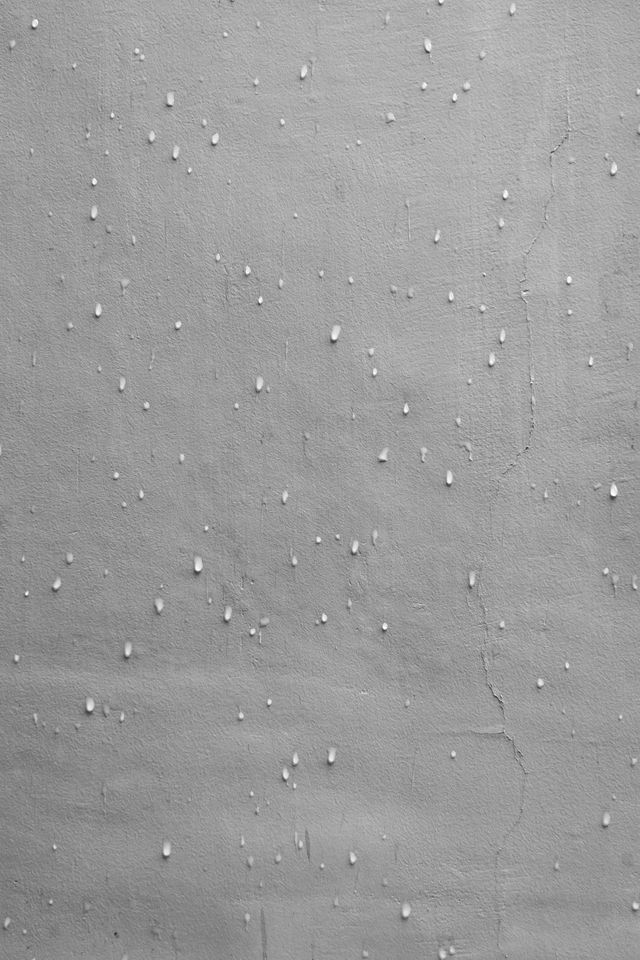 Gray textured wall with scattered small white specks and faint horizontal marks