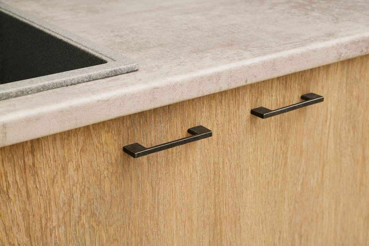 A close up of a kitchen counter with wooden cabinets and black handles.