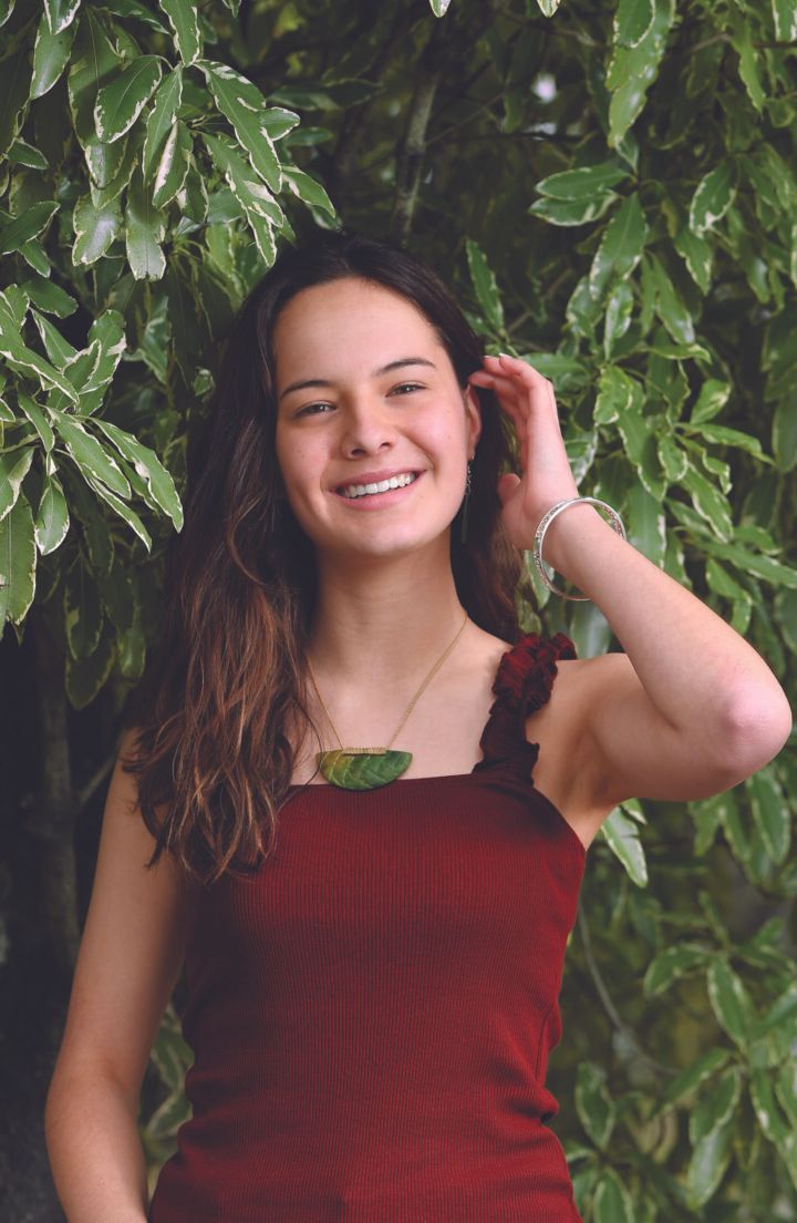 A young woman in a red dress is smiling in front of a tree.