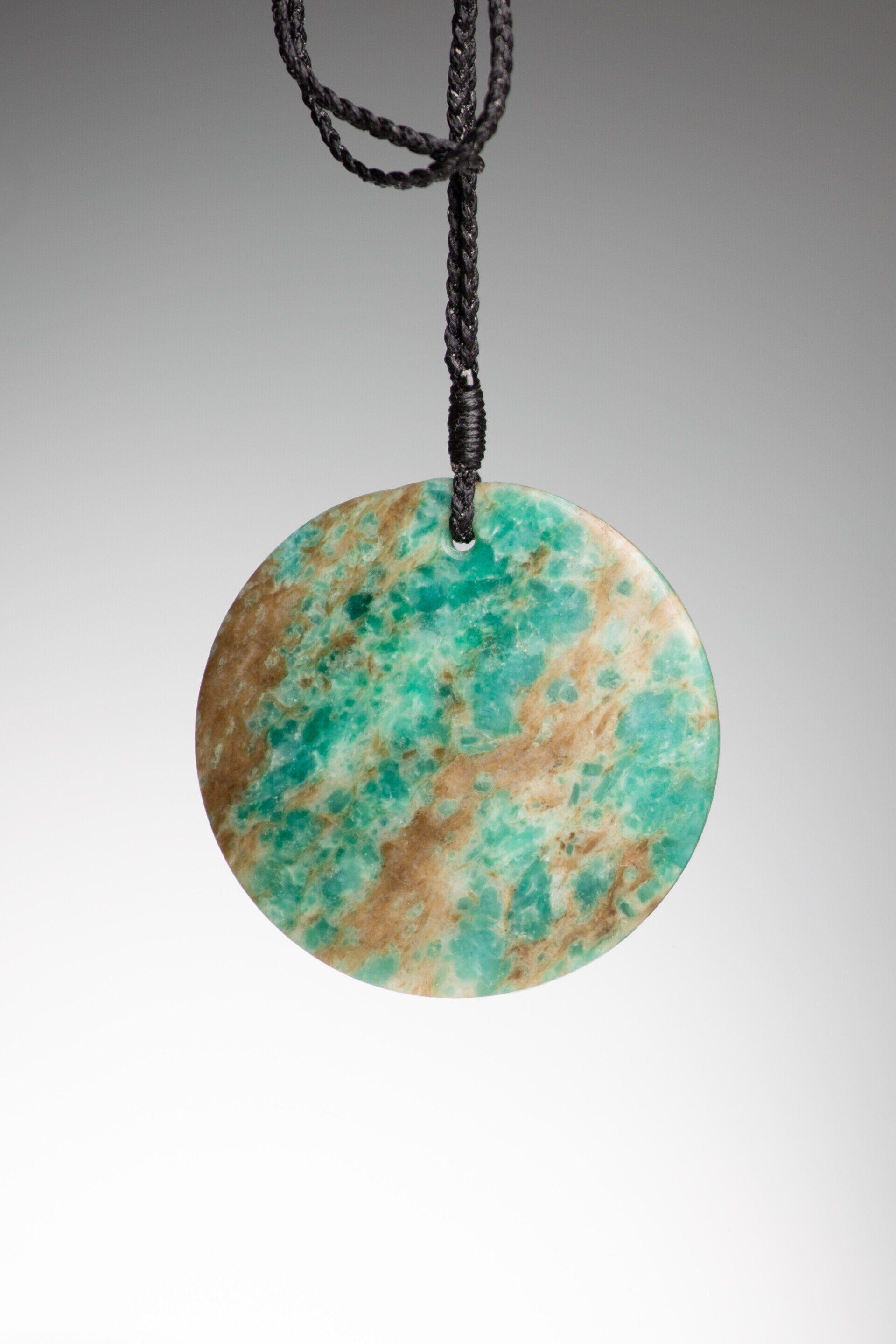 An aotea stone disc shaped pendant is hanging from a black string