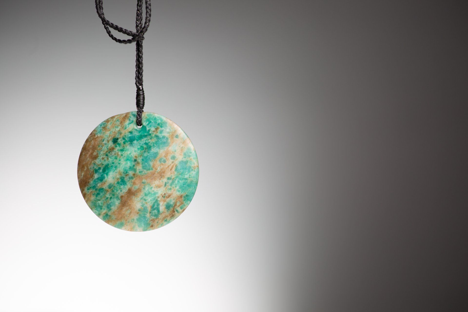 A green and brown pendant is hanging from a black string.