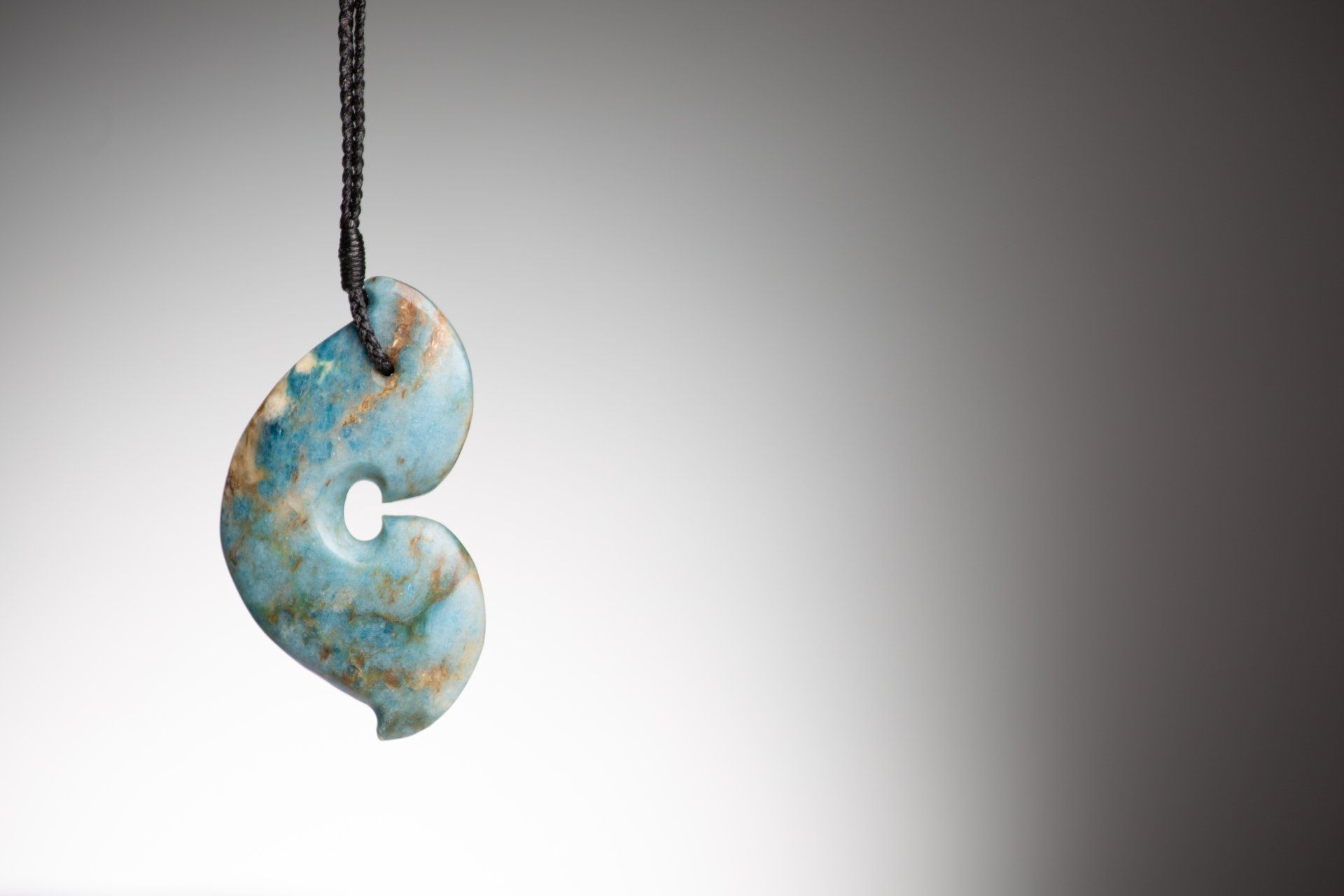 A blue pendant is hanging from a black string on a white background.