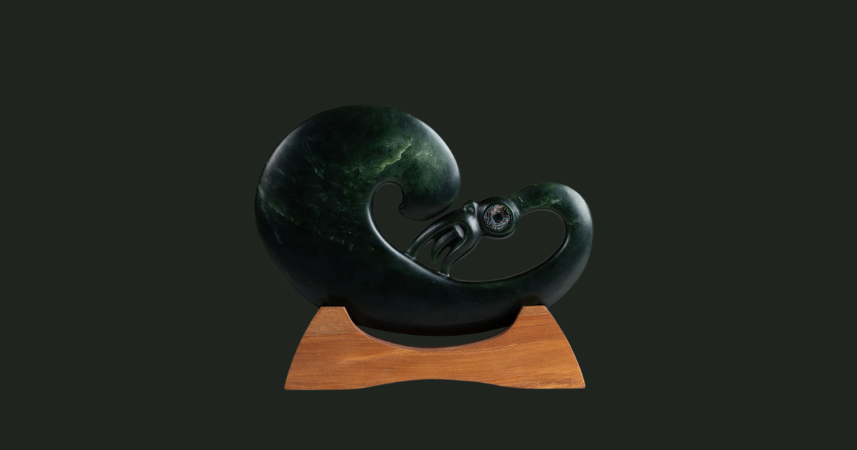 A green pounamu sculpture is sitting on top of a wooden stand.