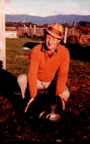 A man in an orange sweater and hat is kneeling down in the dirt.